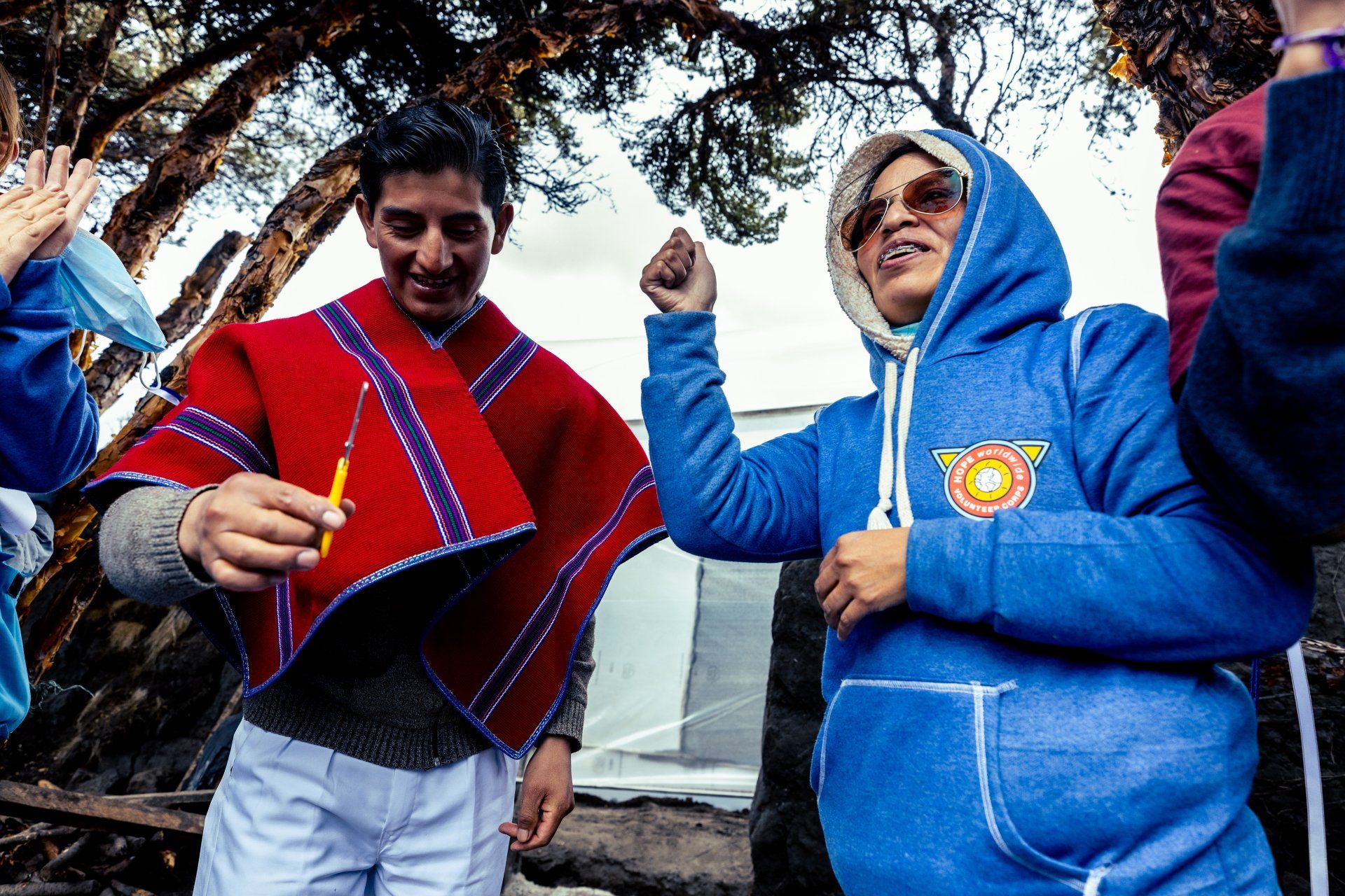 People in blue and red clothing dancing outdoors under trees