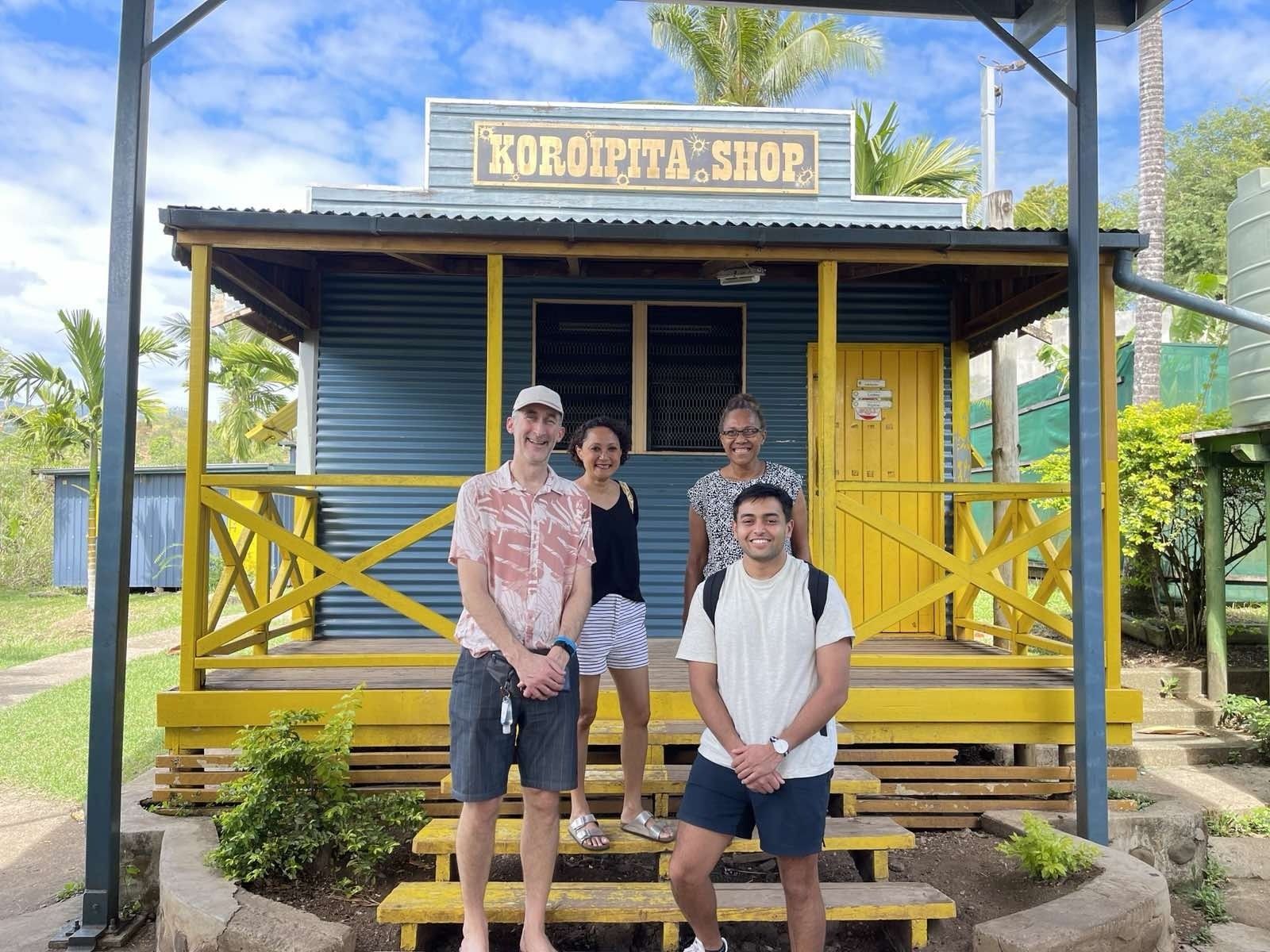 Three people posing in front of a colorful yellow-and-blue café kiosk outdoors