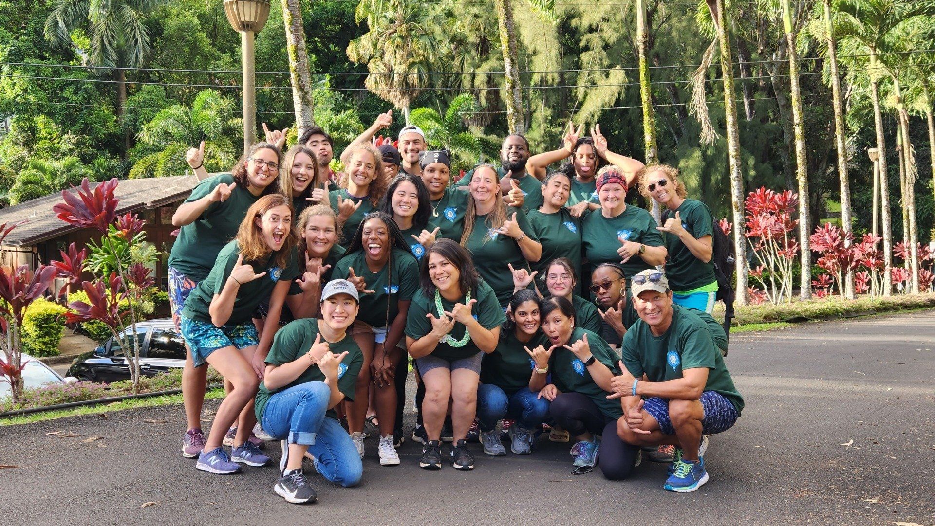 Group of smiling people posing outdoors on a path with lush tropical plants behind them
