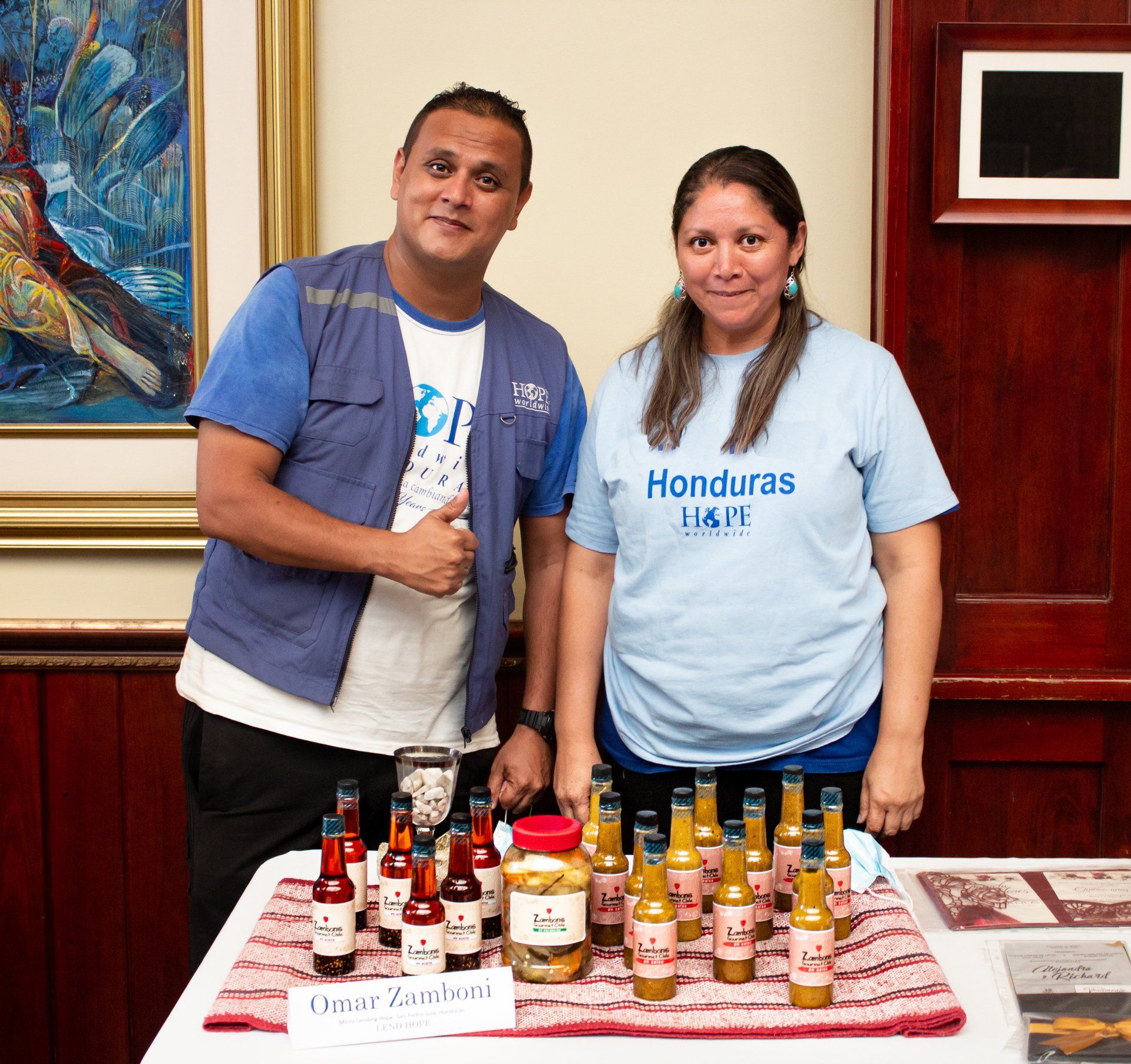 Two people standing behind a table of bottled sauces and condiments at a Honduras event