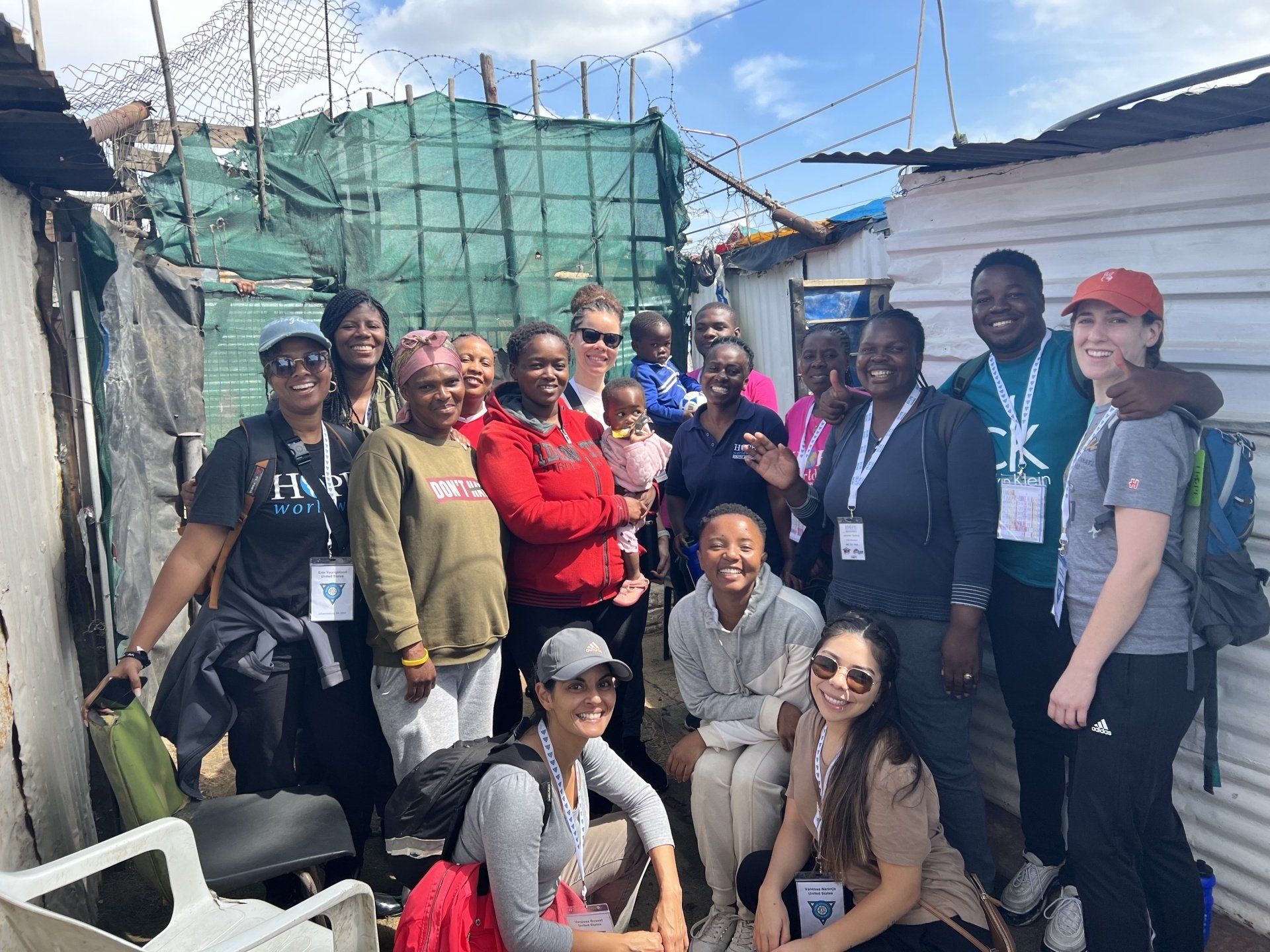 Group of people posing outdoors in a construction area, smiling and wearing lanyards and casual clothes.
