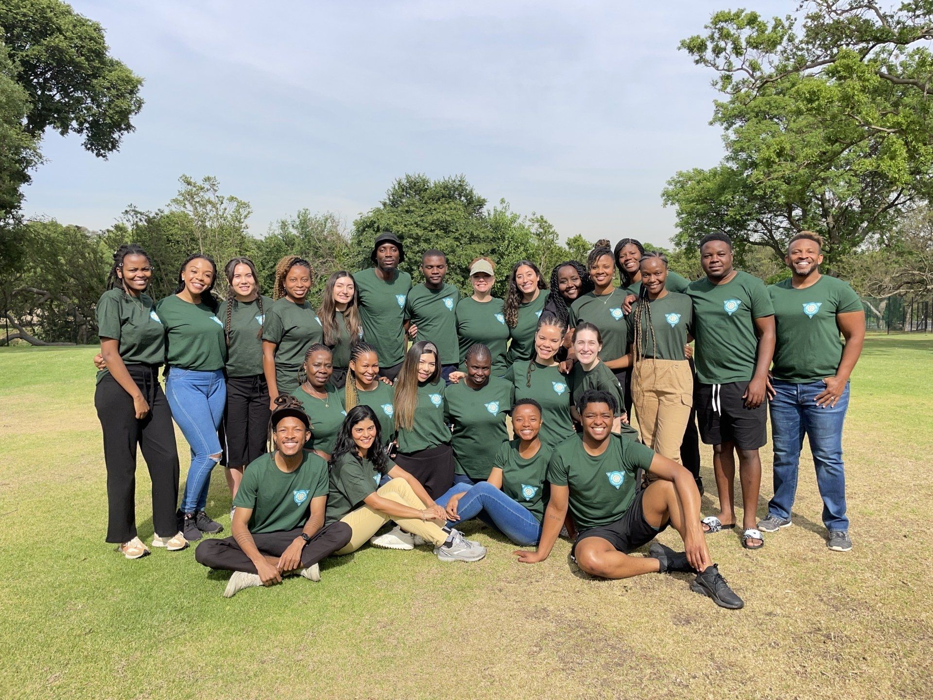 Group of people in green shirts posing together on a grassy field under a bright sky