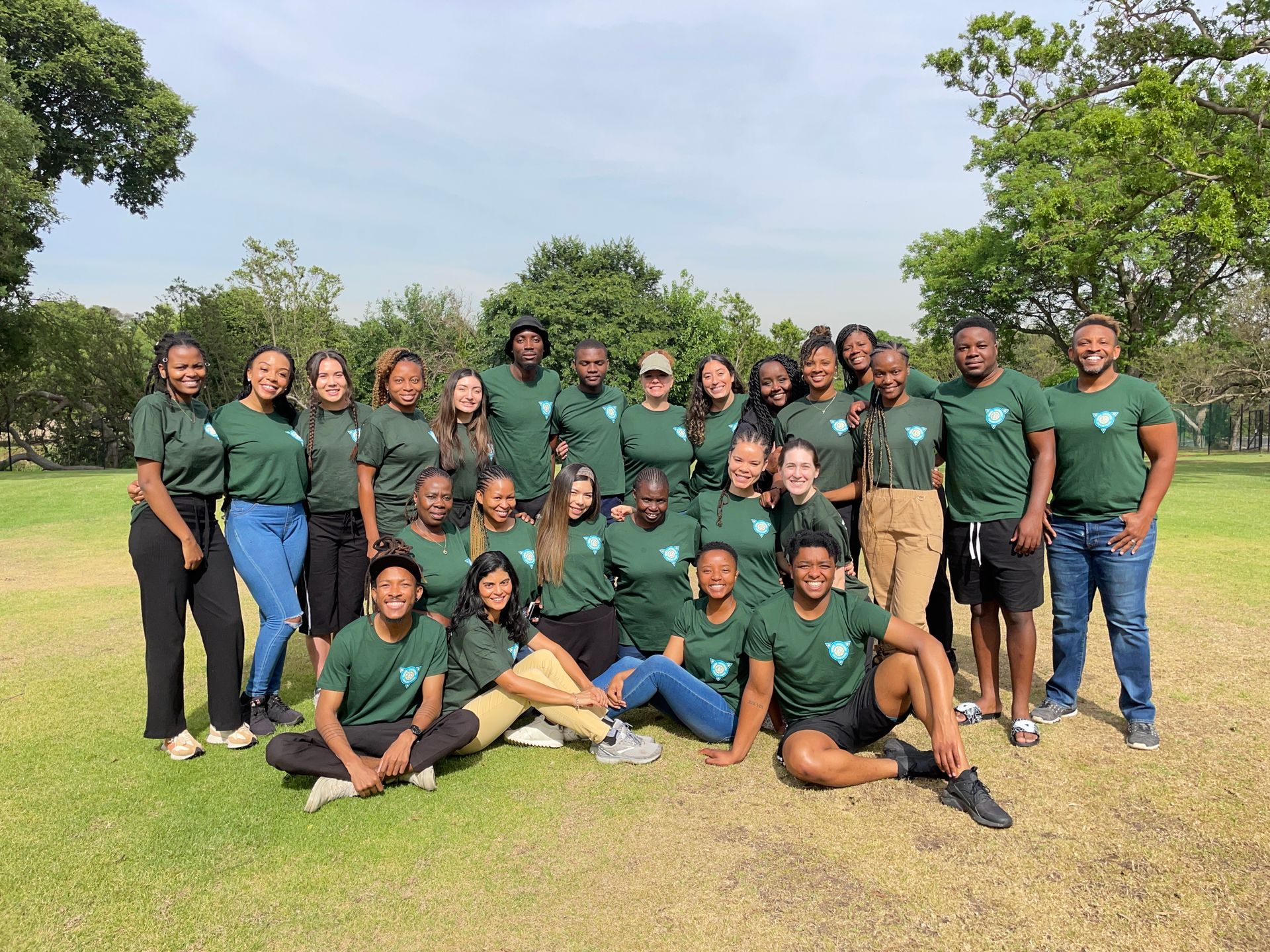 Group of people in matching green shirts posing together outdoors on a sunny grassy field.