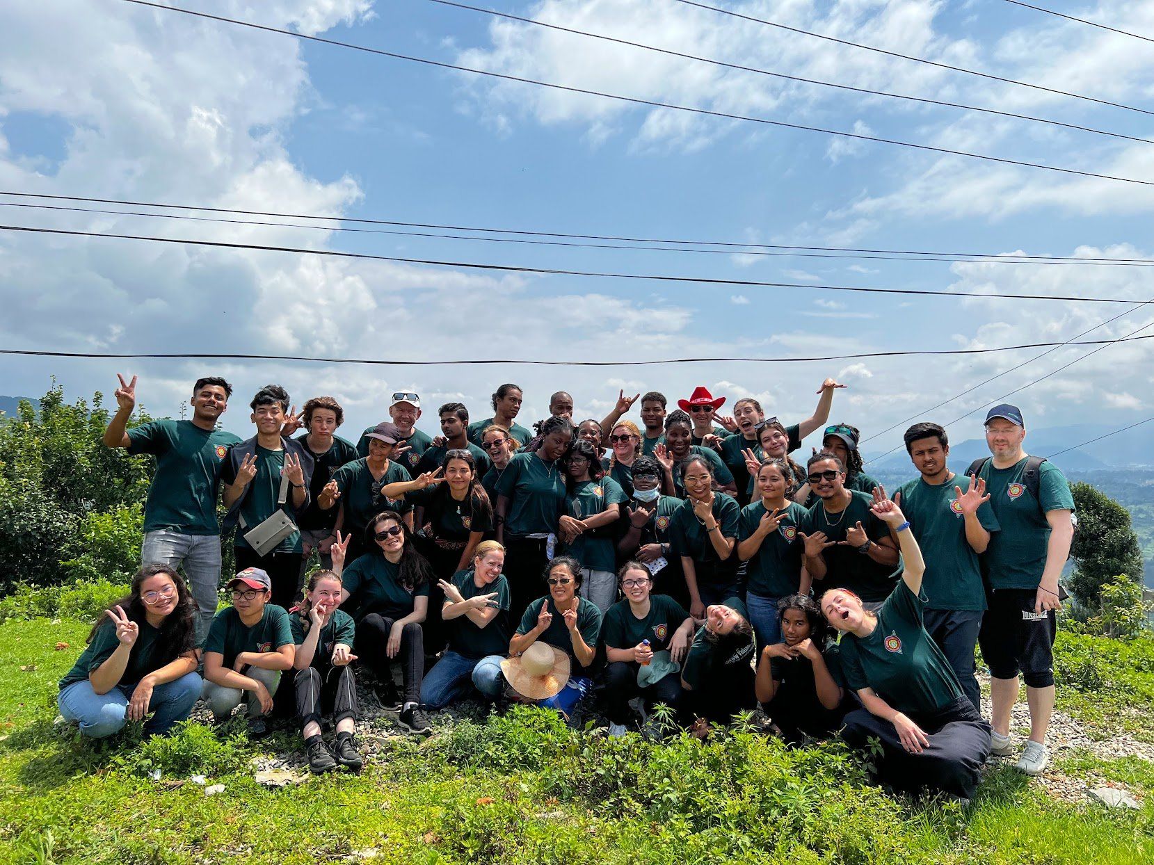Group of people posing outdoors in a field, smiling and raising their arms under a bright sky.