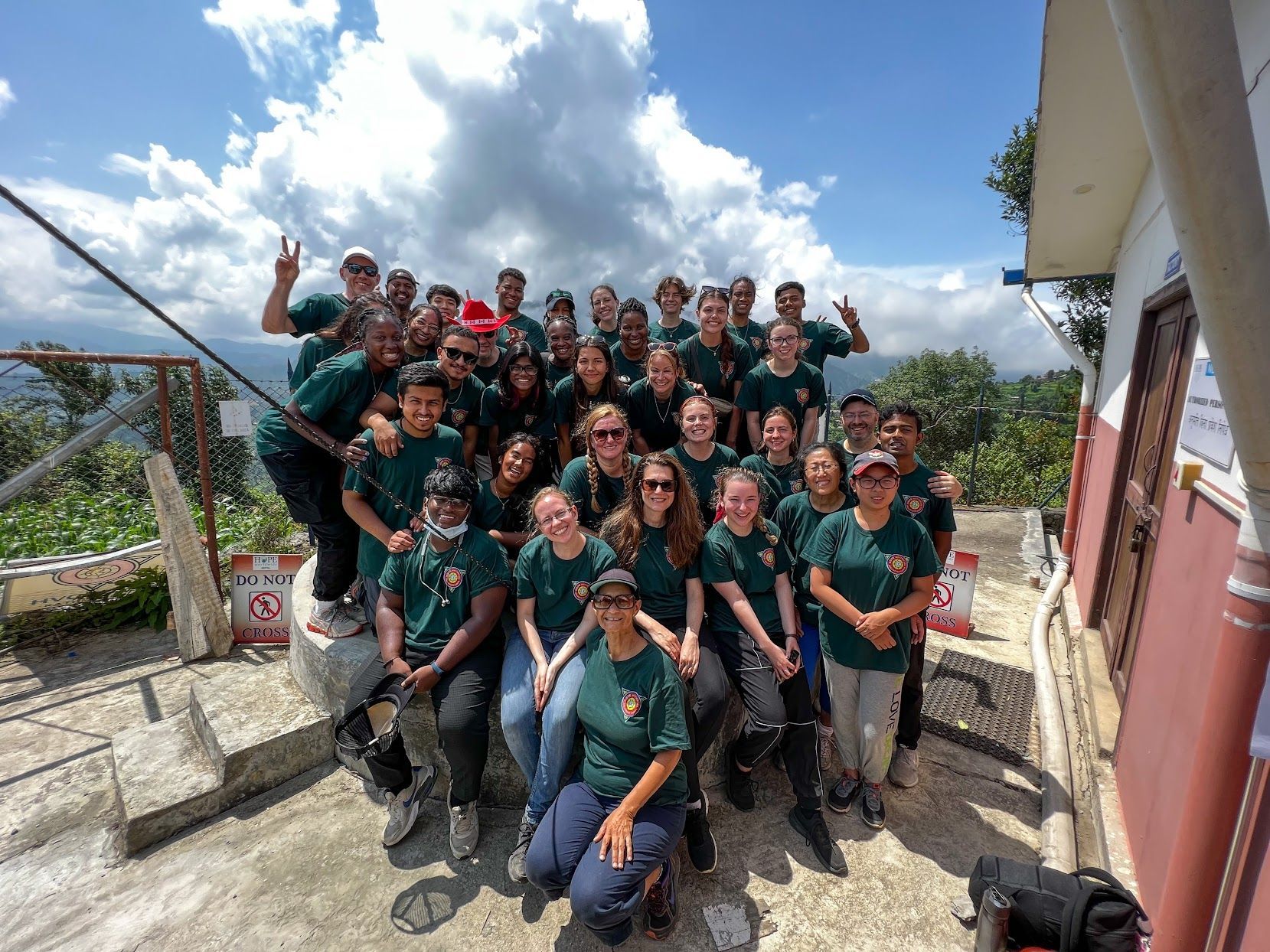 Group of people in green shirts posing outdoors on steps under a bright sky