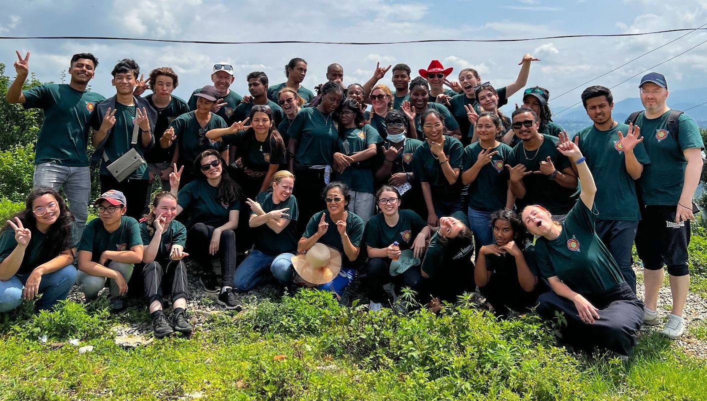 Group of people in dark green shirts posing together outdoors on a sunny grassy hill.