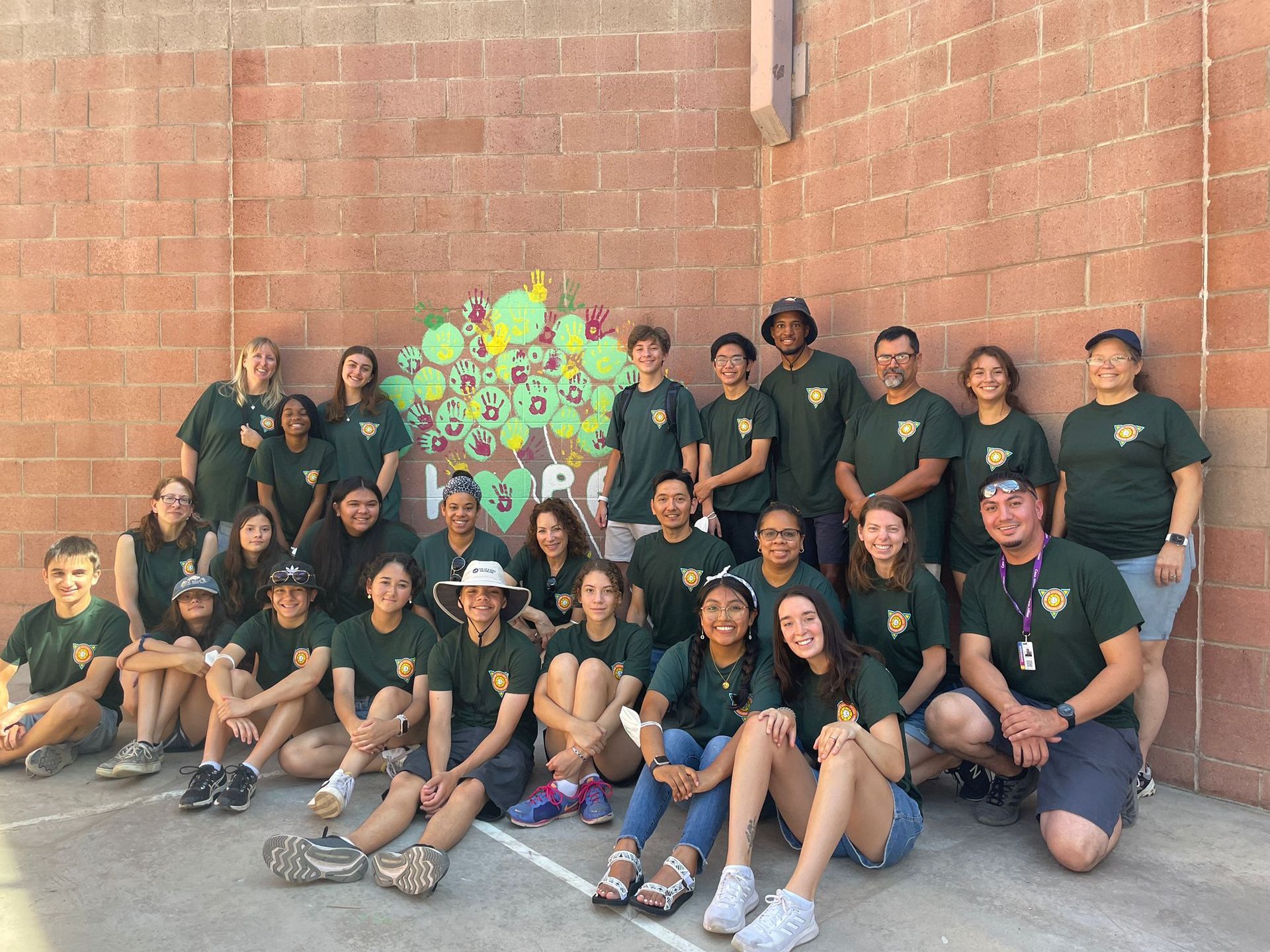 Group of people posing in front of a brick wall with colorful graffiti, seated and standing together outdoors