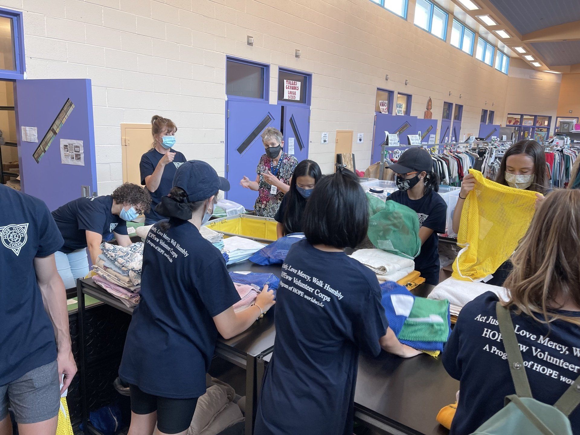 Students gather around tables in a school hallway, sorting colorful materials during a group activity.