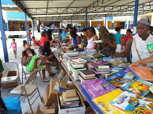 Outdoor book sale under a canopy with tables of books and people browsing and sitting nearby