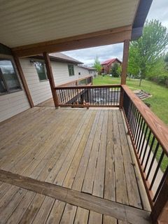 A wooden deck with stairs and a metal railing is in front of a white house.