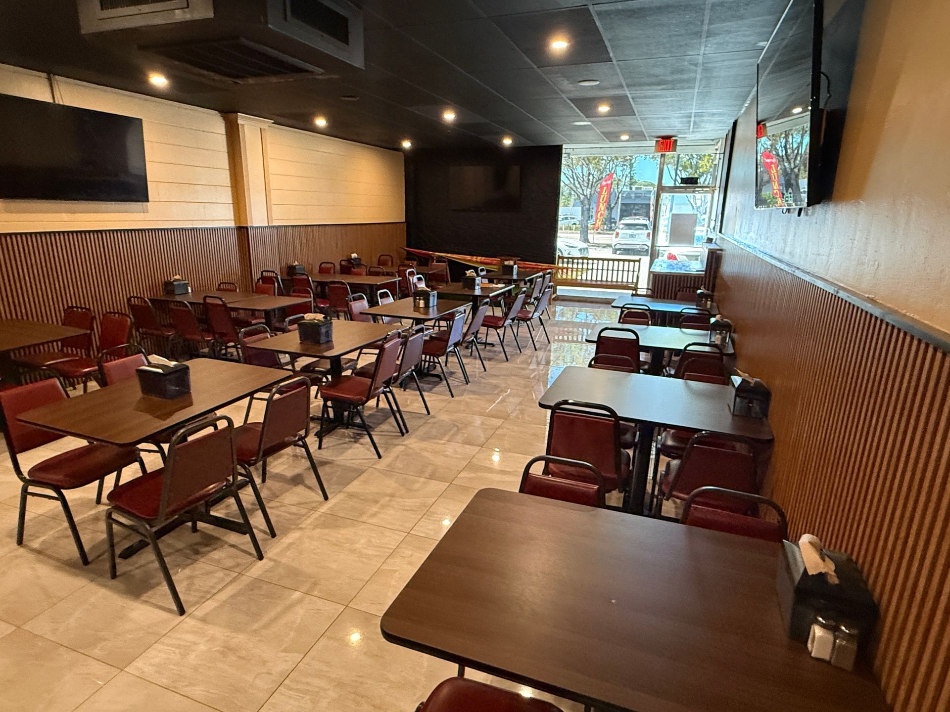 An interior view of a dining room featuring rows of dark wood tables and red chairs on a light tiled floor.