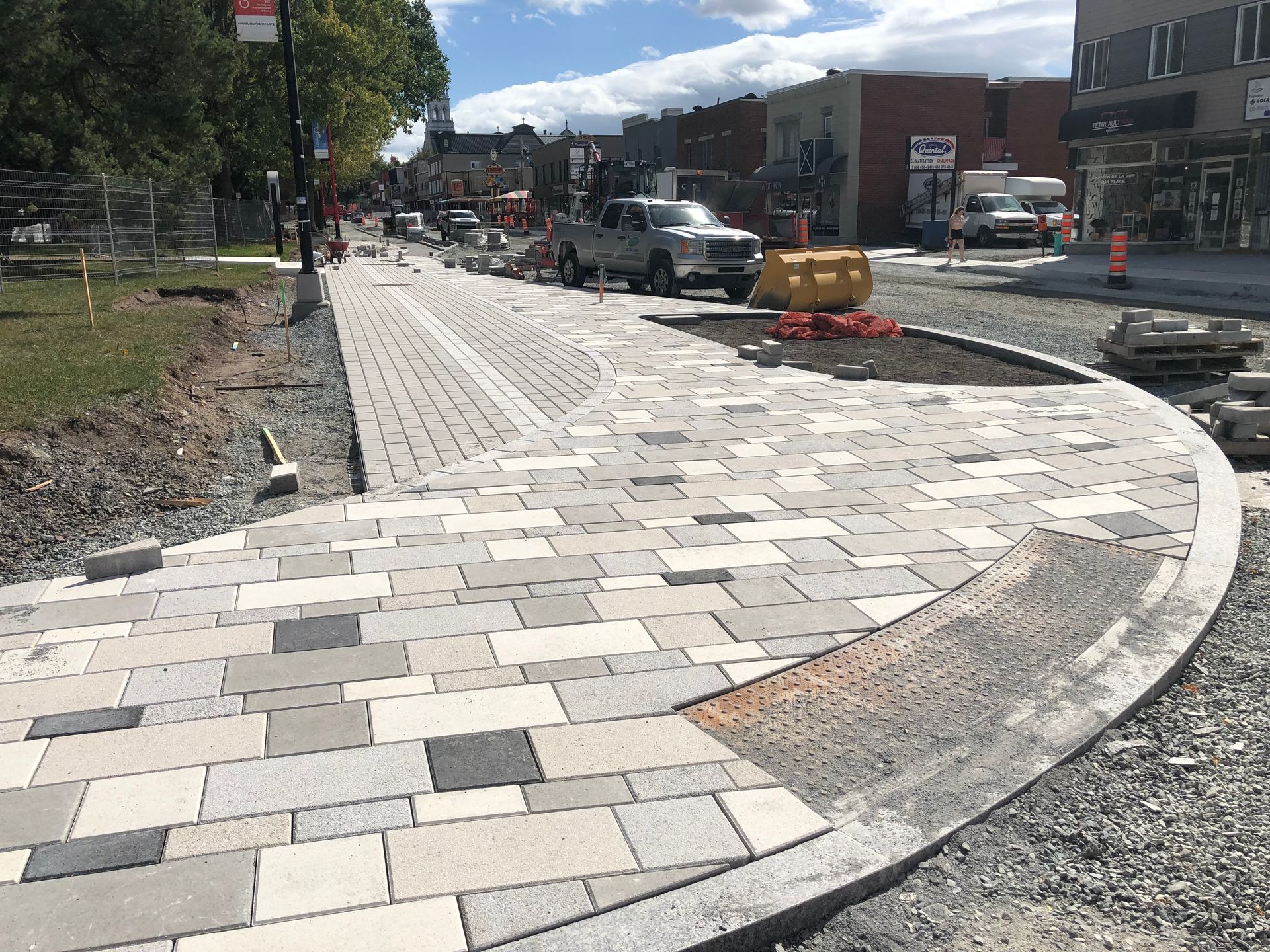 Construction d'un trottoir : pavés multicolores et bordure dans une rue de la ville sous un ciel bleu.