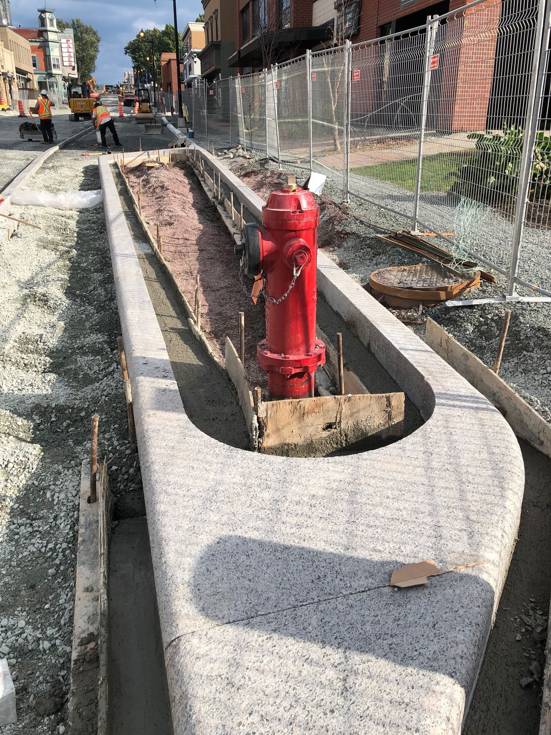 Travaux de voirie : une borne d’incendie rouge se trouve dans une tranchée en béton remplie de gravier, à côté d’un trottoir en construction.