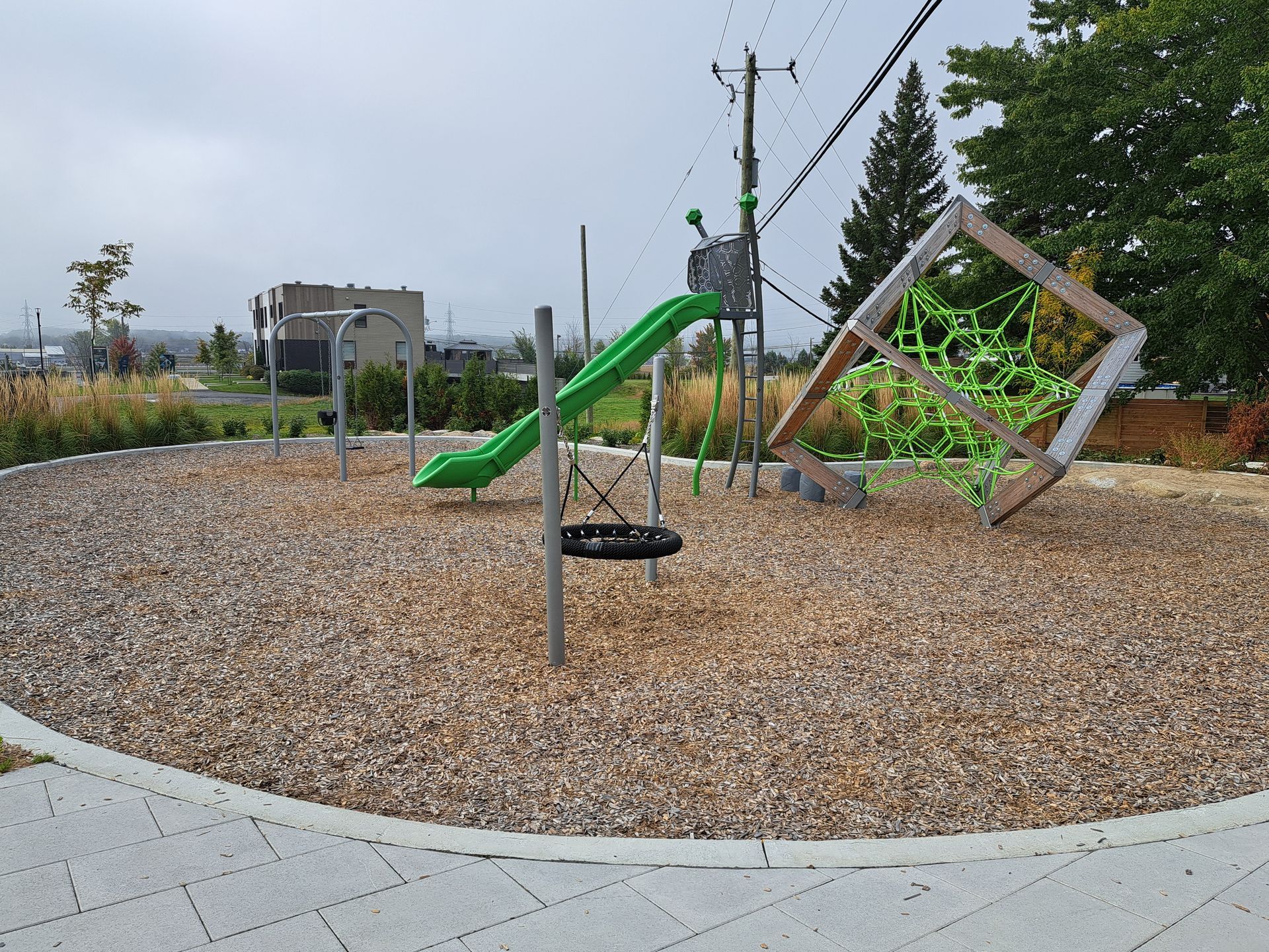 Aire de jeux avec toboggan vert, structure d'escalade et revêtement de sol en copeaux de bois.