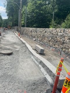 Travaux routiers : Bordure et muret en pierre en construction ; cônes orange et ruban de signalisation.