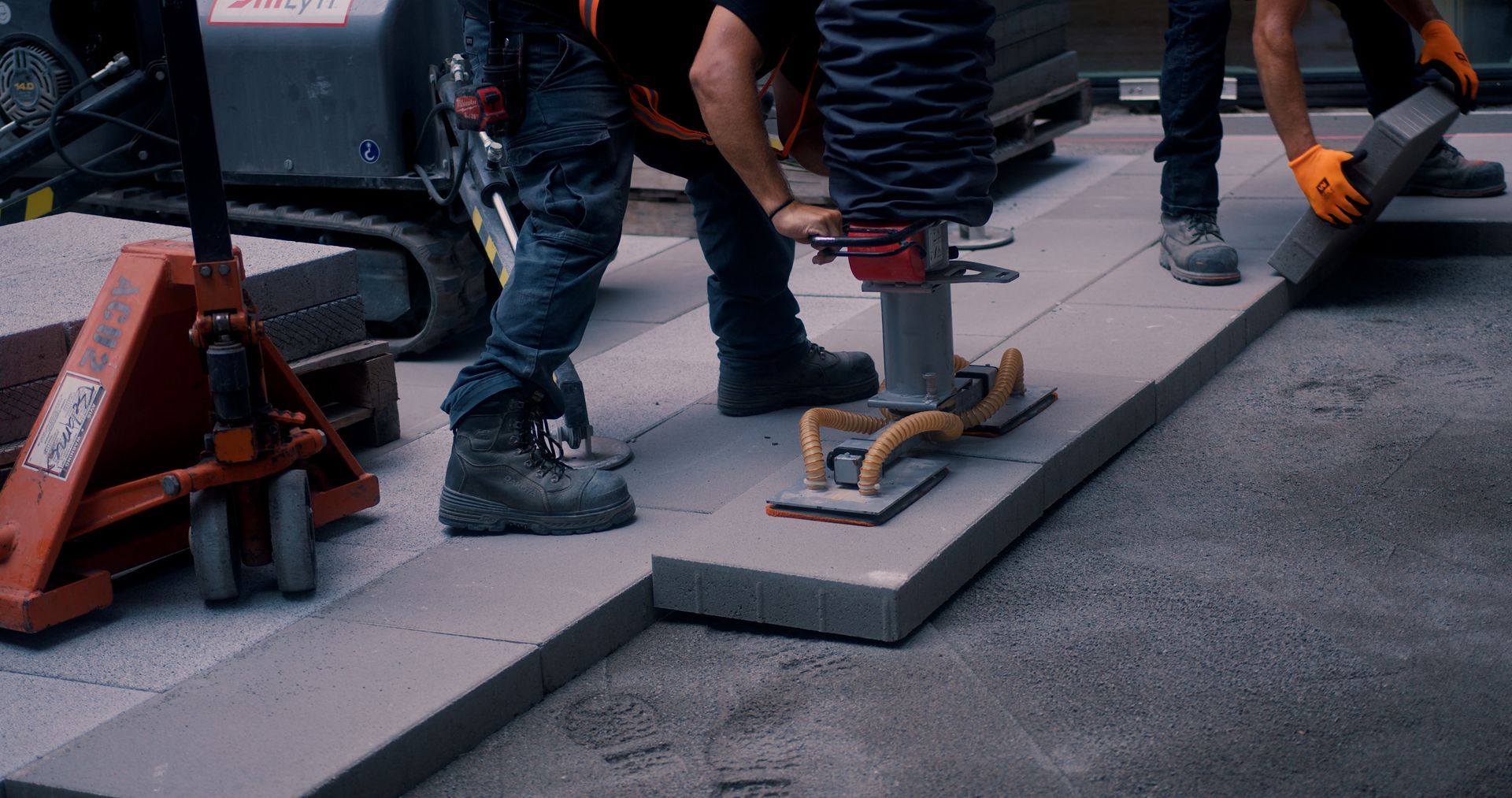 Des ouvriers utilisent un outil de levage pour poser un grand pavé gris sur une rue.