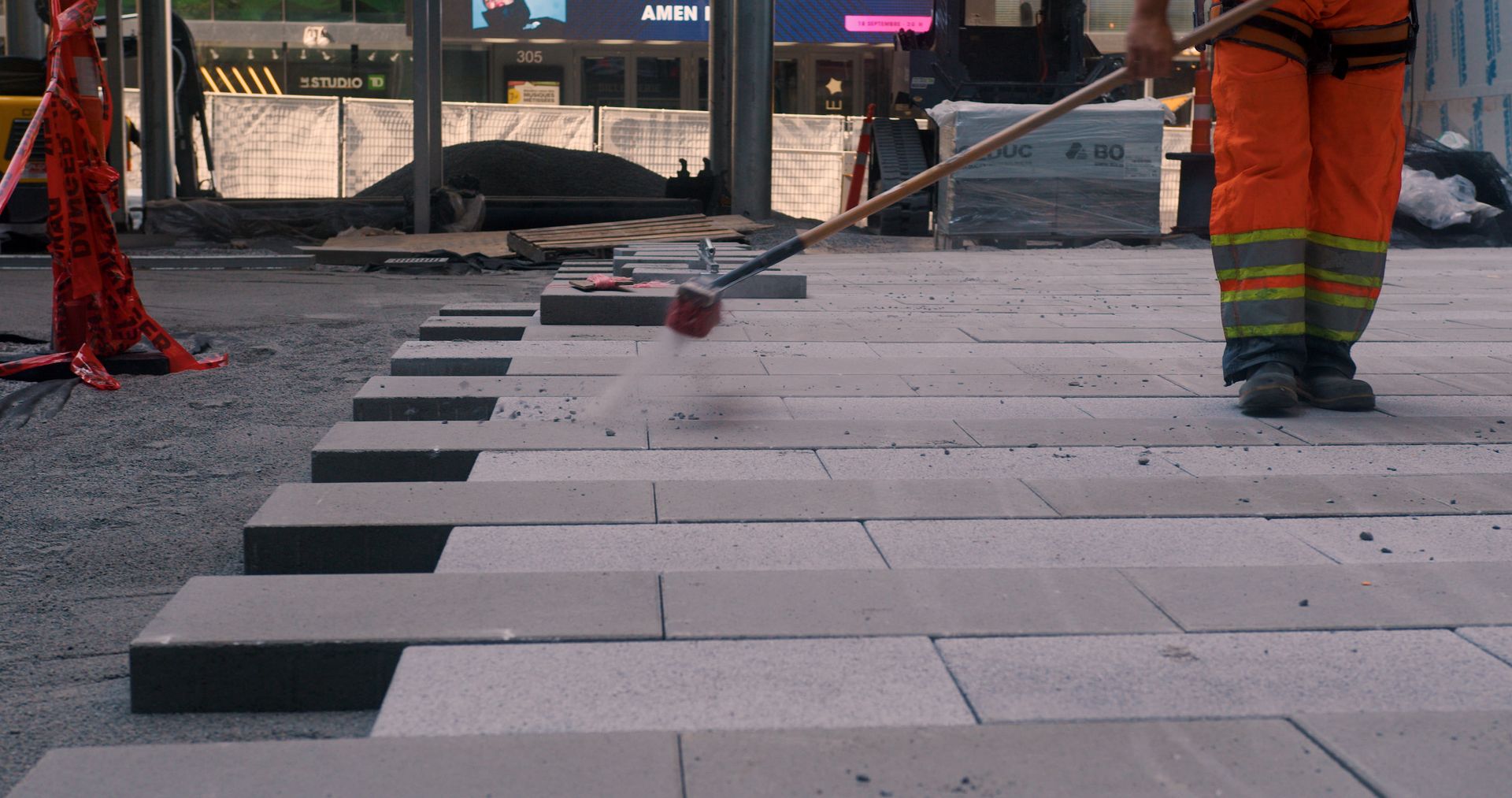 Un ouvrier du bâtiment balaie des fines particules entre les pavés d'un trottoir.