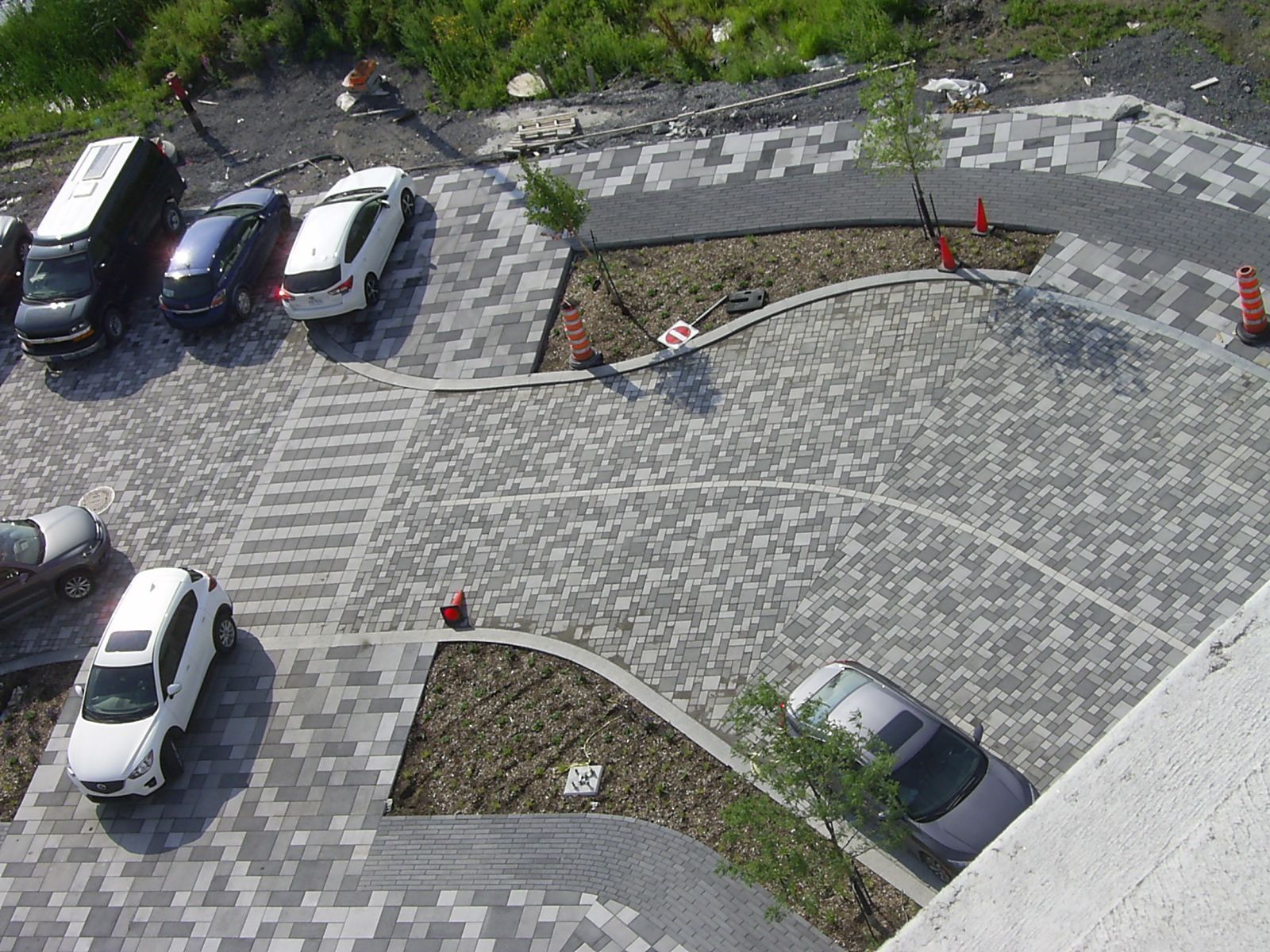 Vue aérienne d'un parking pavé de briques grises, avec des voitures garées et des espaces aménagés.