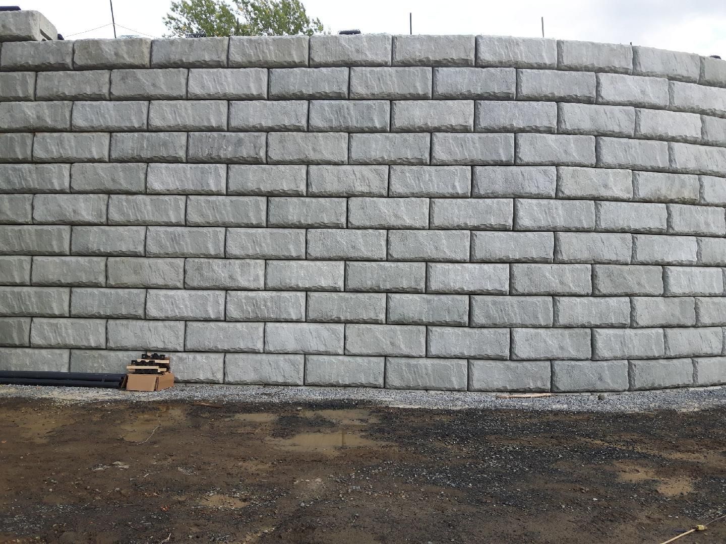 Mur de soutènement incurvé, construit en blocs rectangulaires gris, se détachant sur un ciel nuageux.