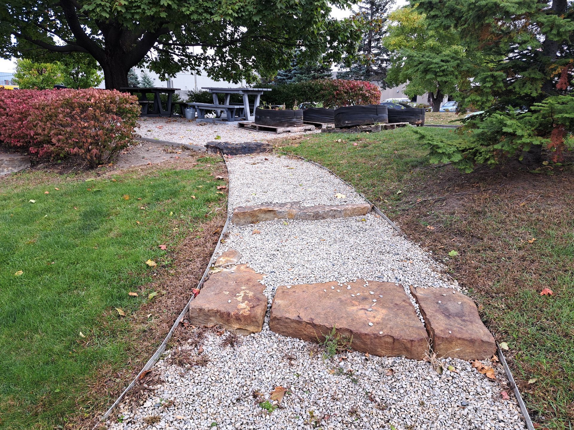 Chemin de pierres traversant un jardin paysager avec pelouse et buissons.