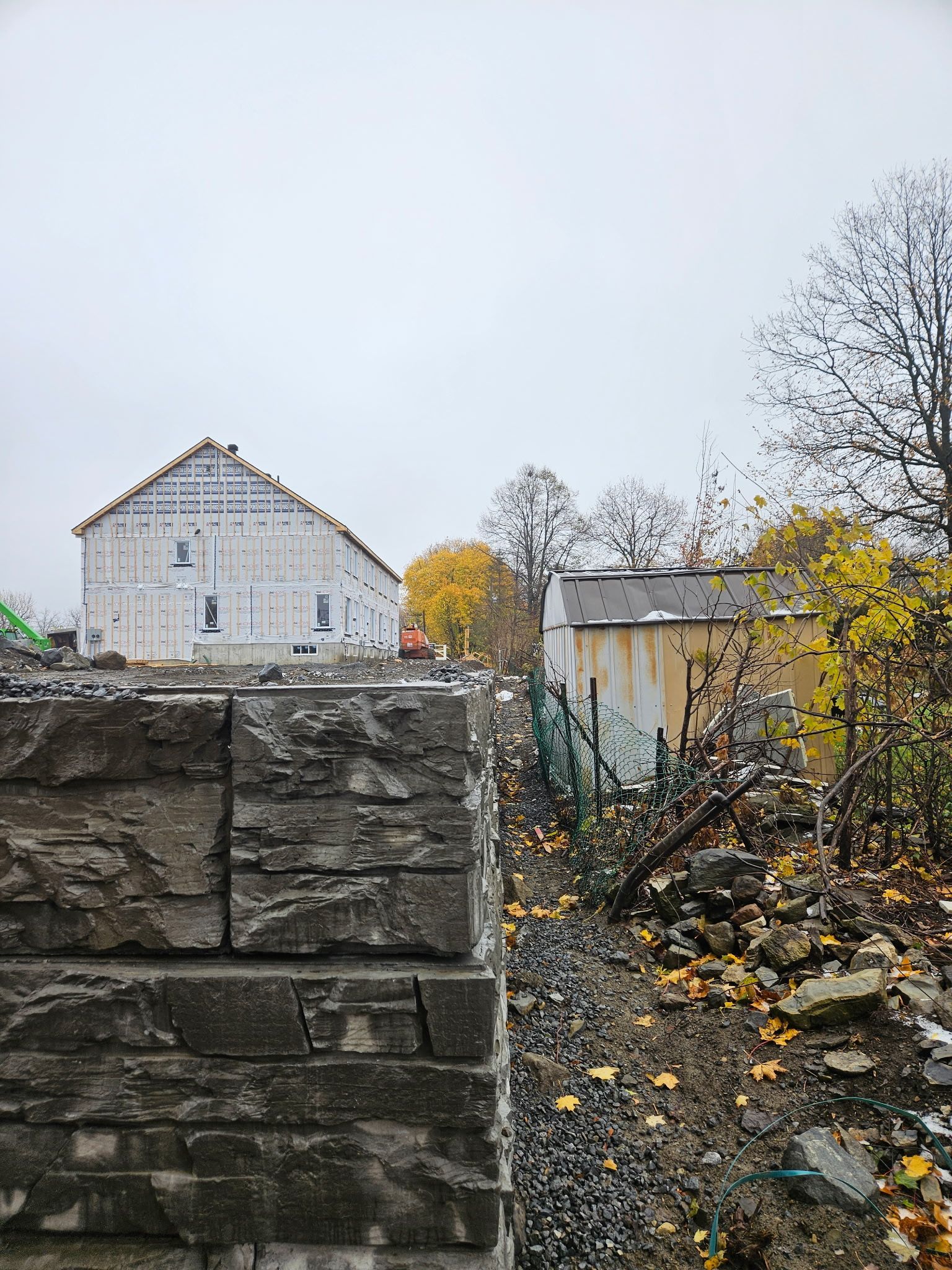 Bâtiment en construction derrière un mur de pierre. Journée nuageuse avec des couleurs d'automne.