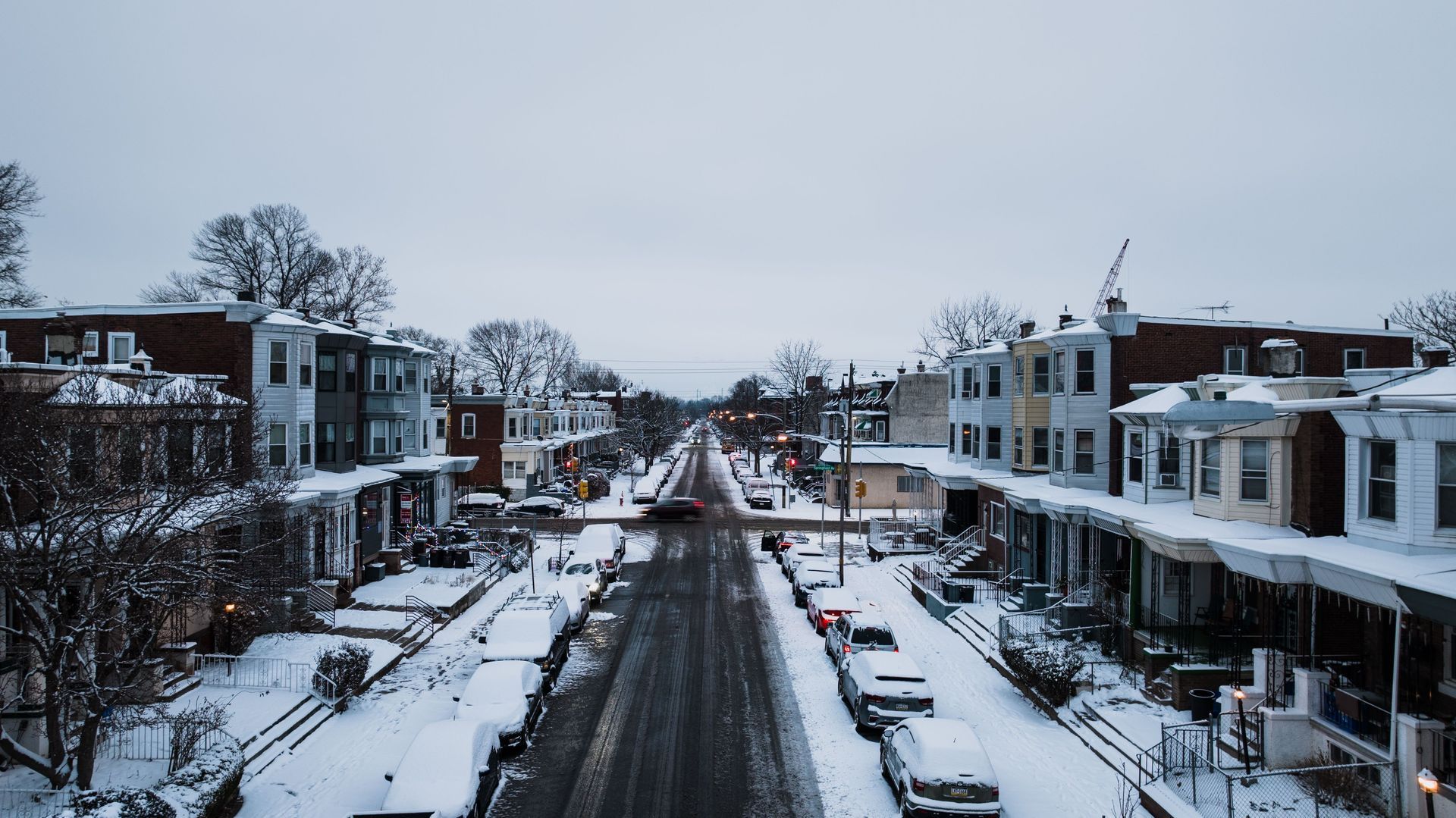 Vue en hauteur d'une rue r&eacute;sidentielle enneig&eacute;e bord&eacute;e de maisons et de voitures stationn&eacute;es.