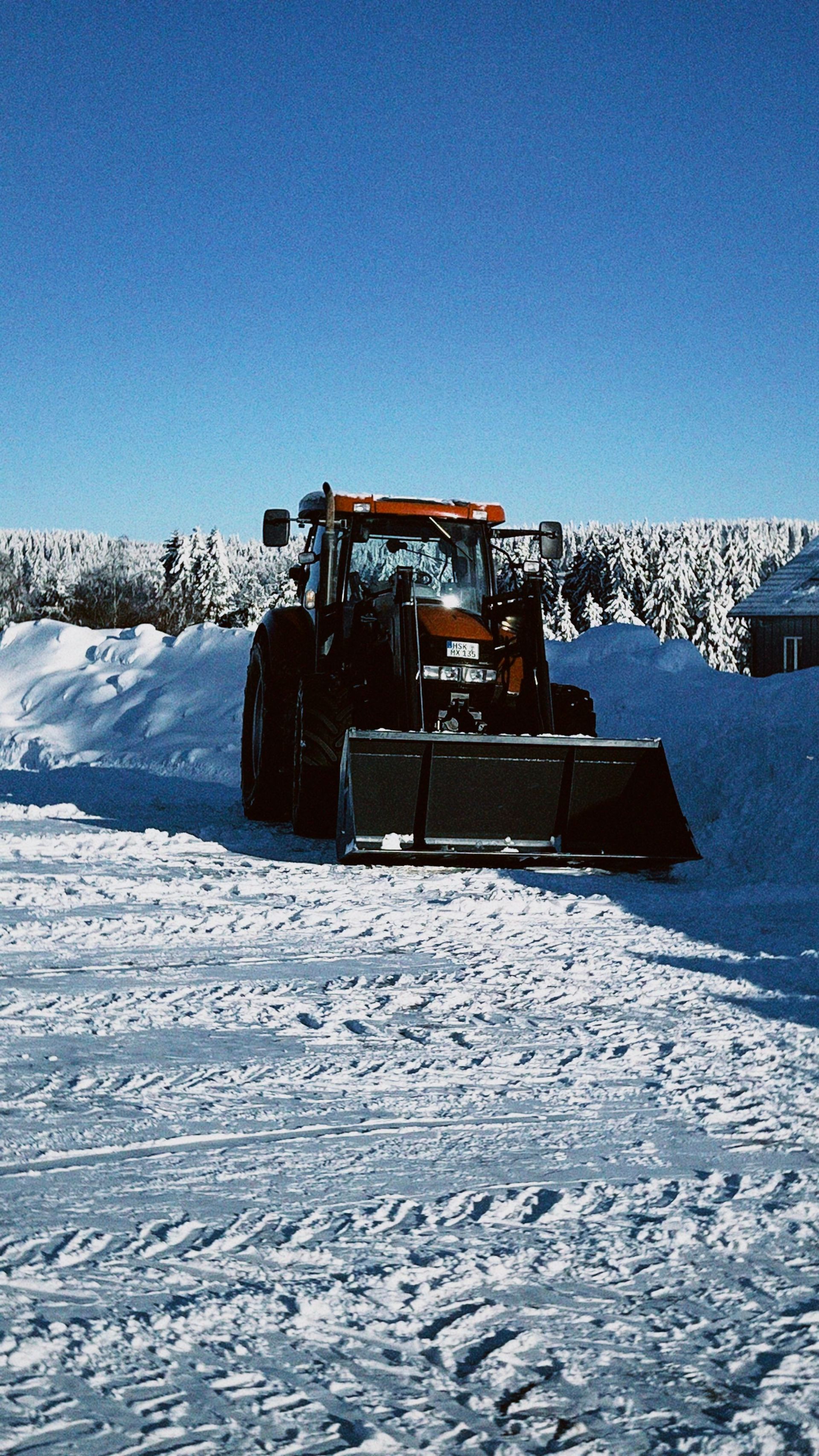 Tracteur de d&eacute;neigement sur une surface enneig&eacute;e sous un ciel bleu.