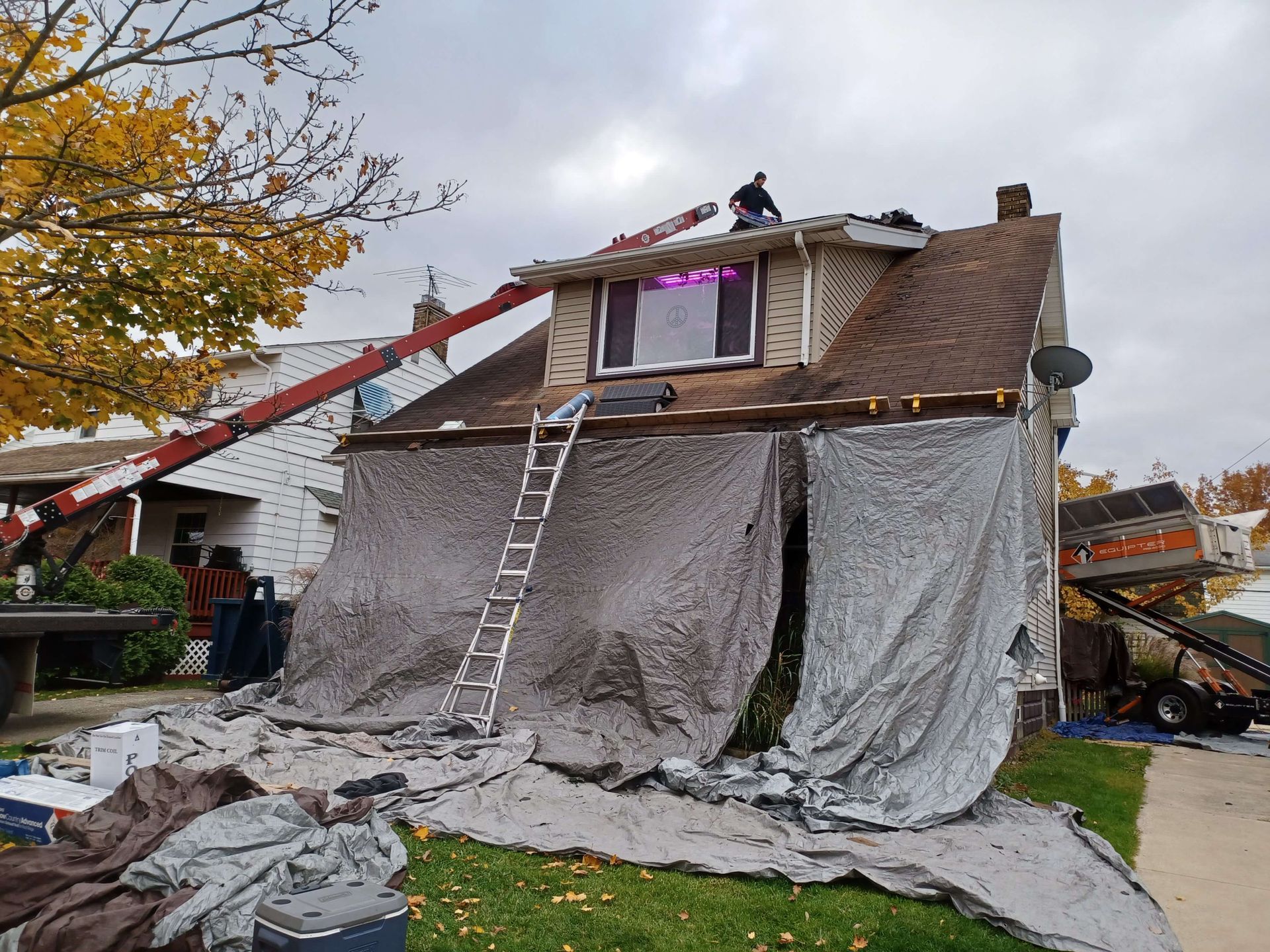 Workers on a roof covering a damaged house with gray tarp and a ladder during repairs