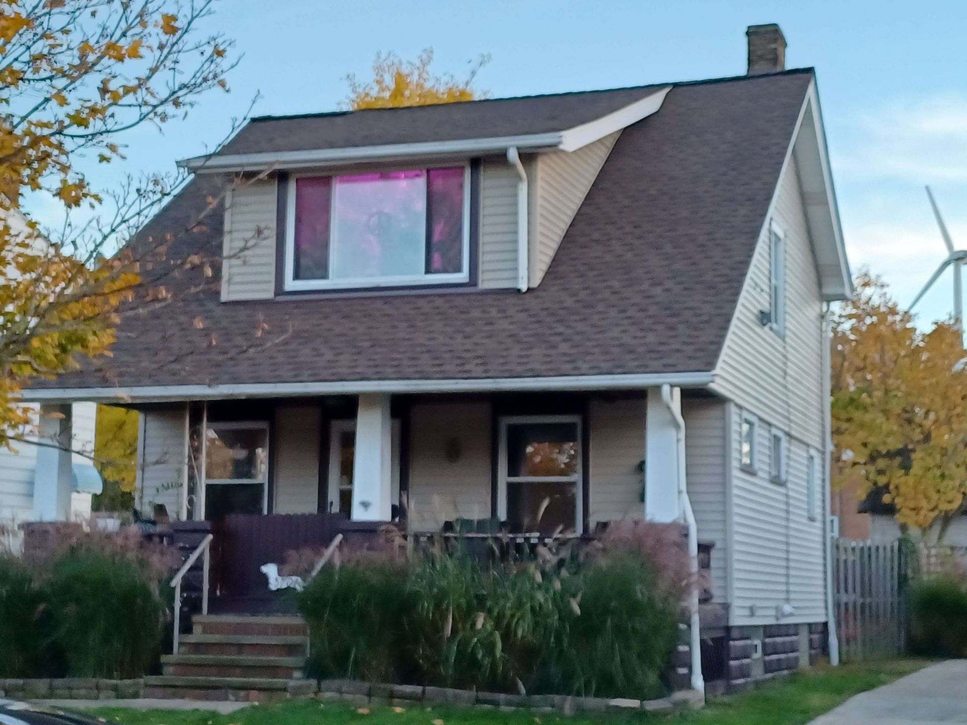 Two-story beige house with a brown roof, front porch, and pink-lit upstairs window at dusk