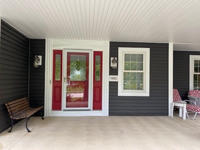 Front porch with red front door, dark gray siding, white trim, bench, and small seating area.