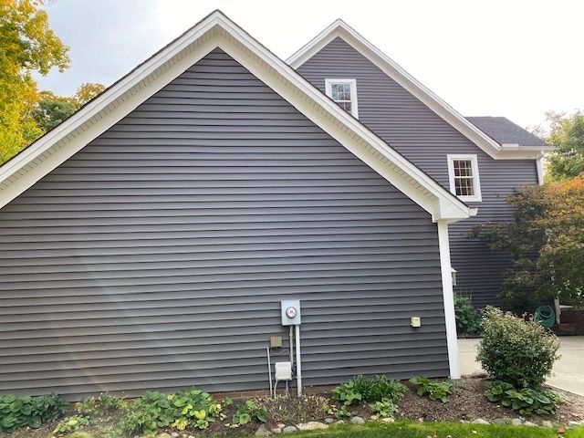 Gray house exterior with white trim, gabled roof, and small windows, viewed from the side.