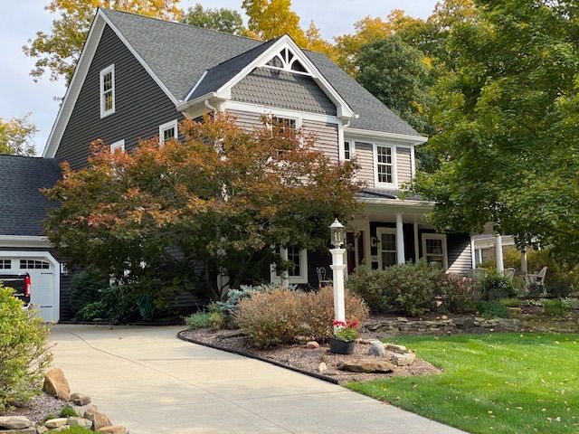 Two-story gray house with a driveway, porch, and autumn trees in front