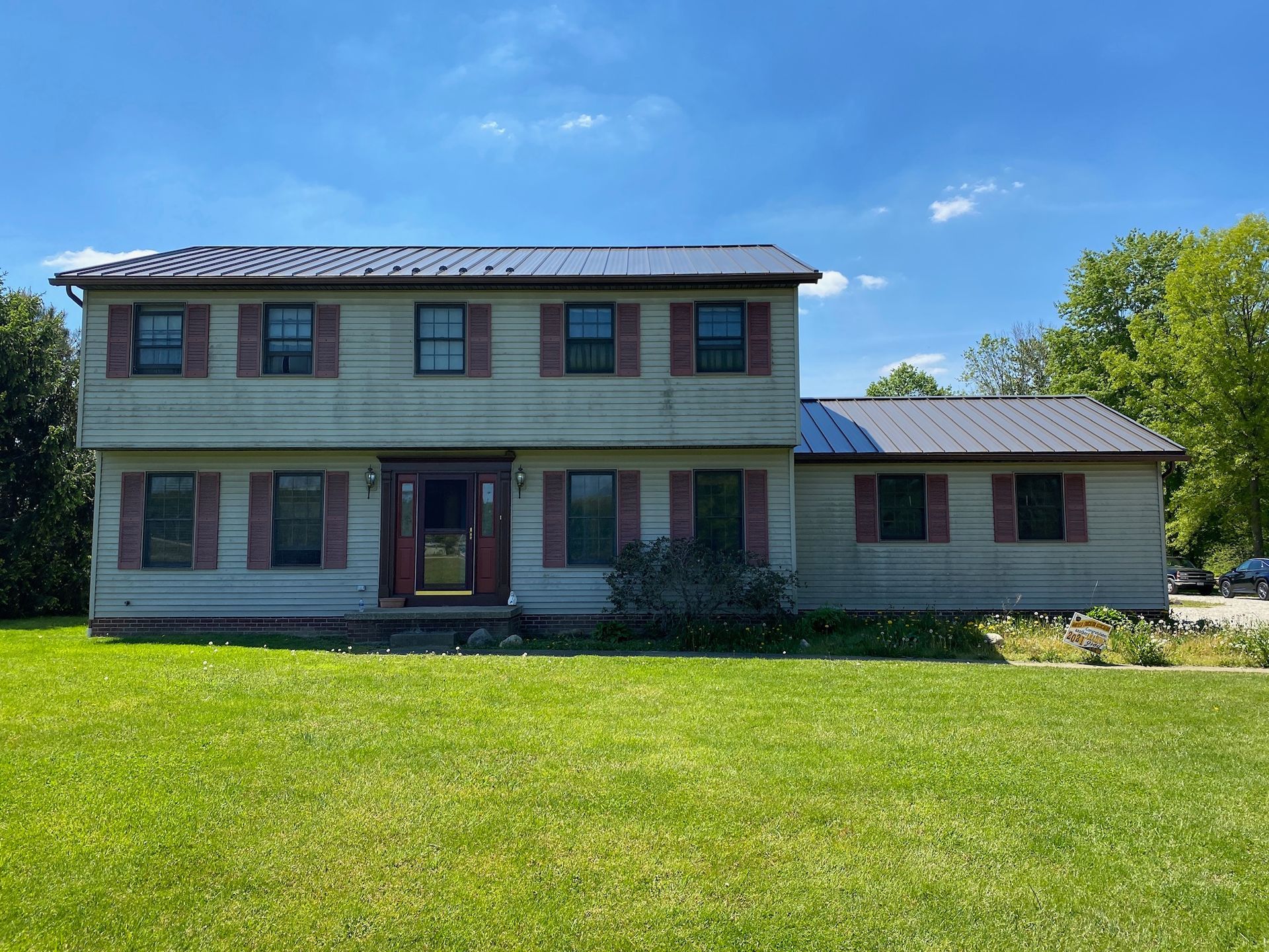 Two-story house with gray siding, red shutters, and a wide green lawn under a blue sky
