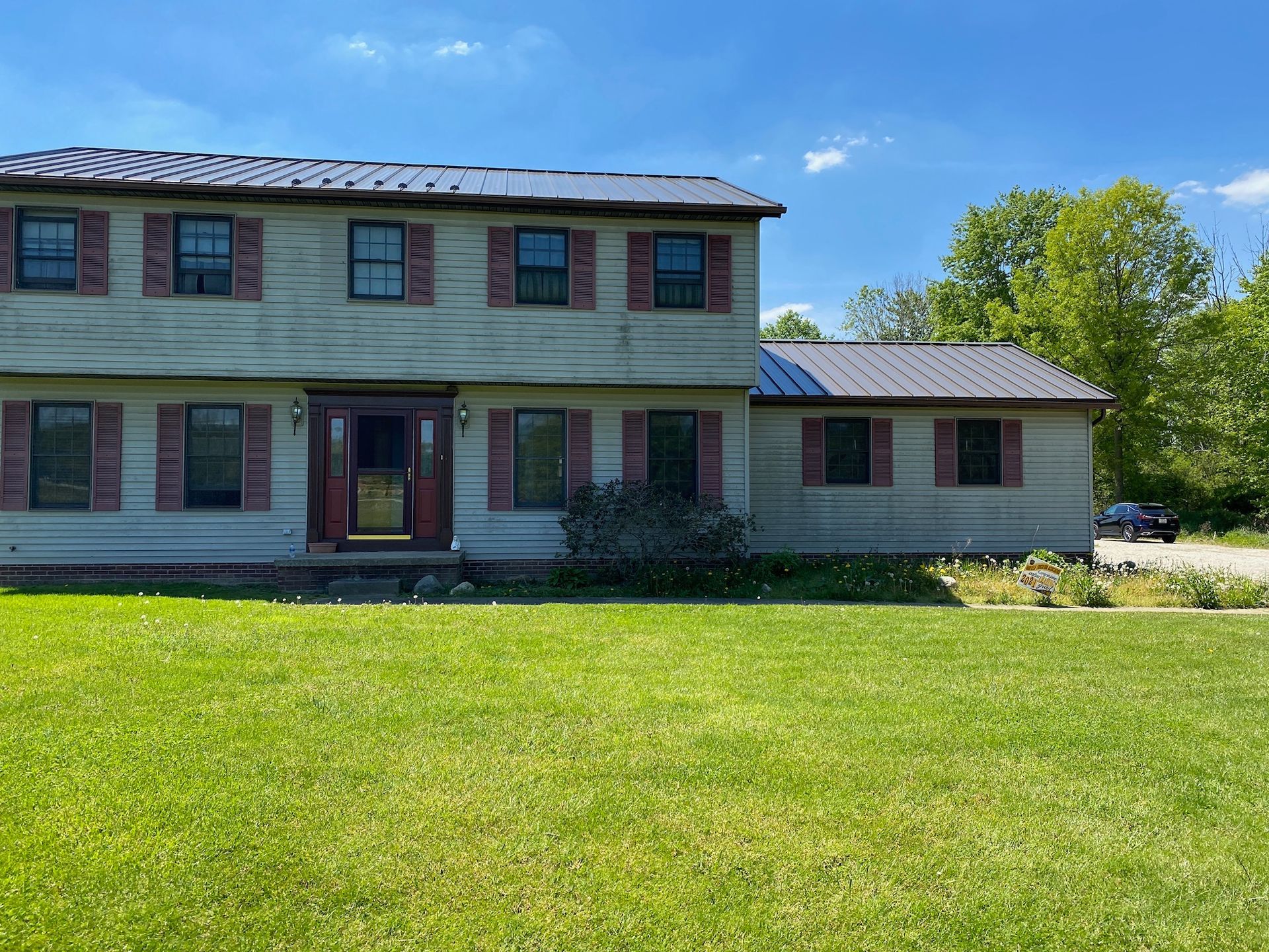 Two-story farmhouse with green siding, a front porch, and a large grassy yard under a blue sky.
