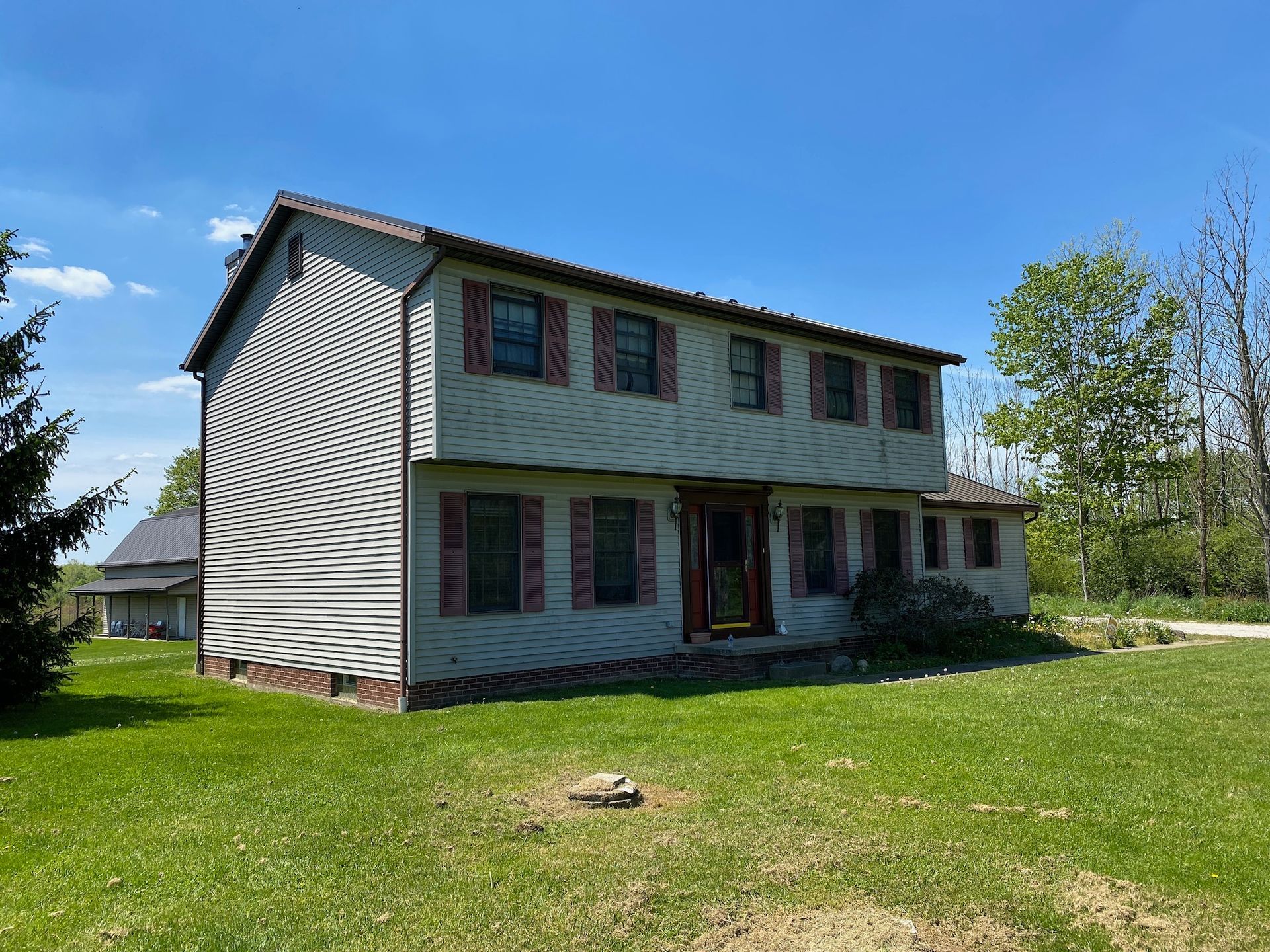 Two-story white house with red shutters and a front porch, set on a green lawn under a blue sky