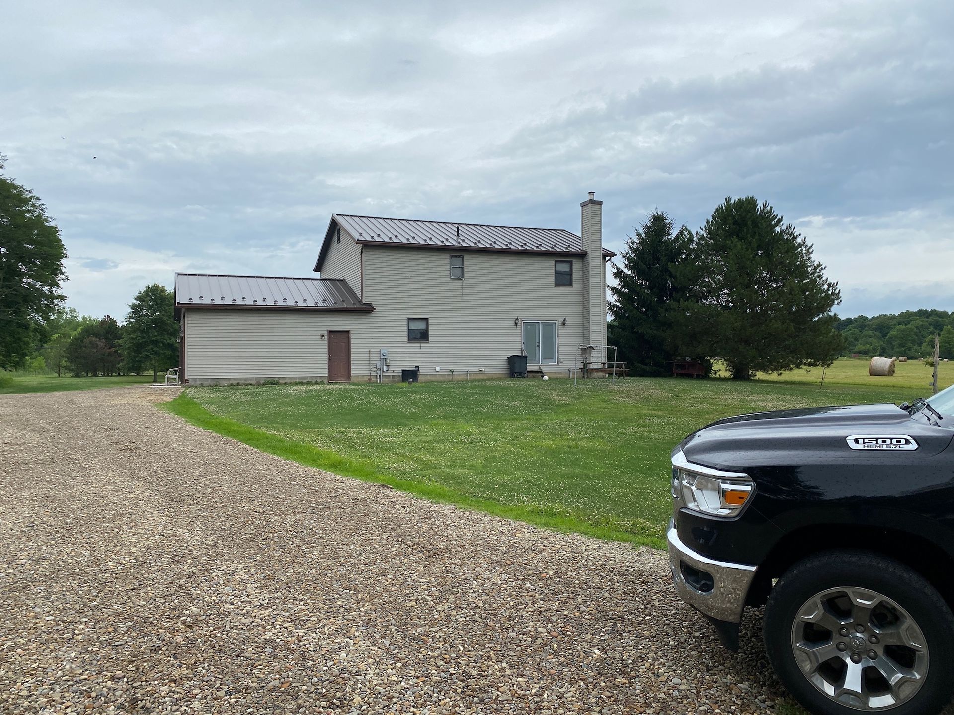 Rural beige house with gravel driveway, grass yard, and black pickup truck in foreground