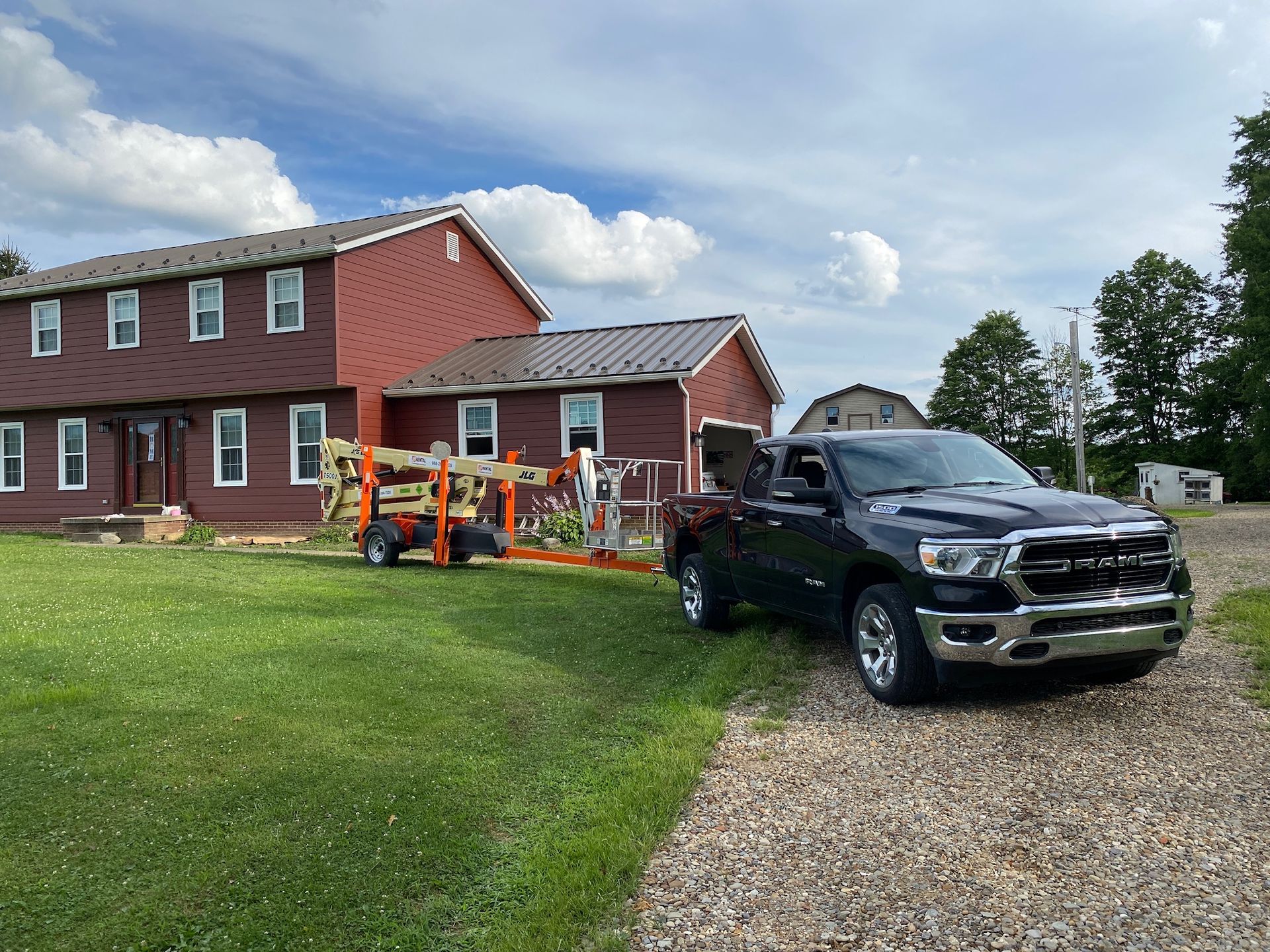 Black pickup truck parked on gravel beside a red house, with orange lawn equipment on the grass.