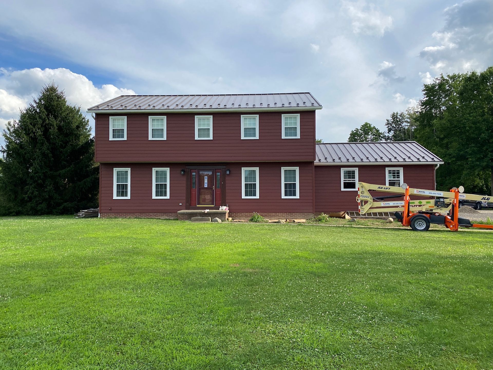 Two-story red house with white trim and a grassy yard, under a cloudy sky.