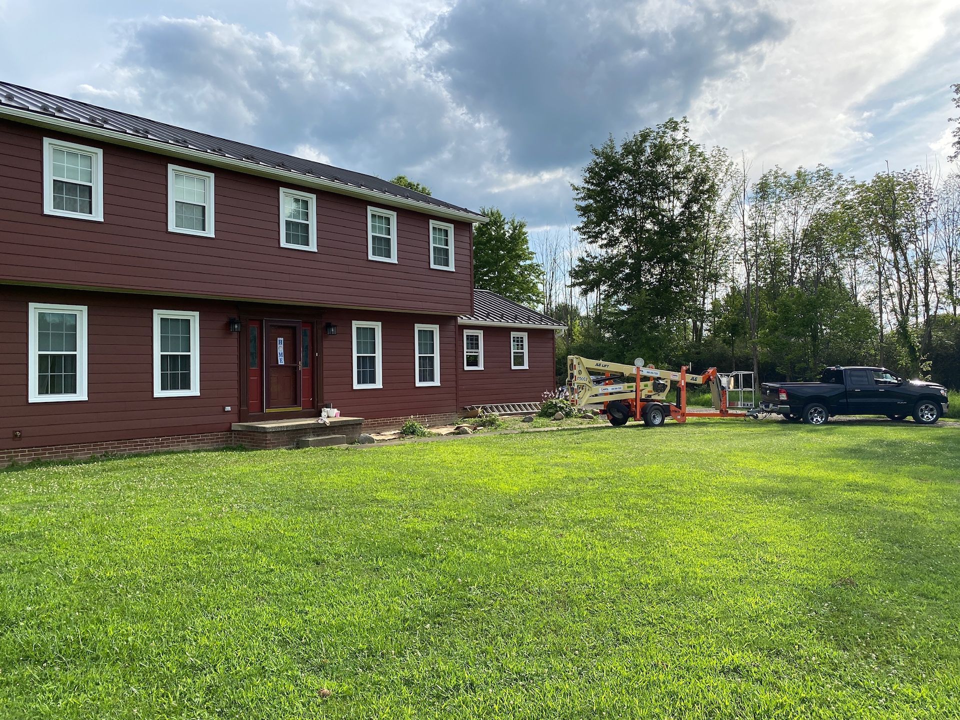 Red two-story house with white trim on a grassy lot under a cloudy sky.