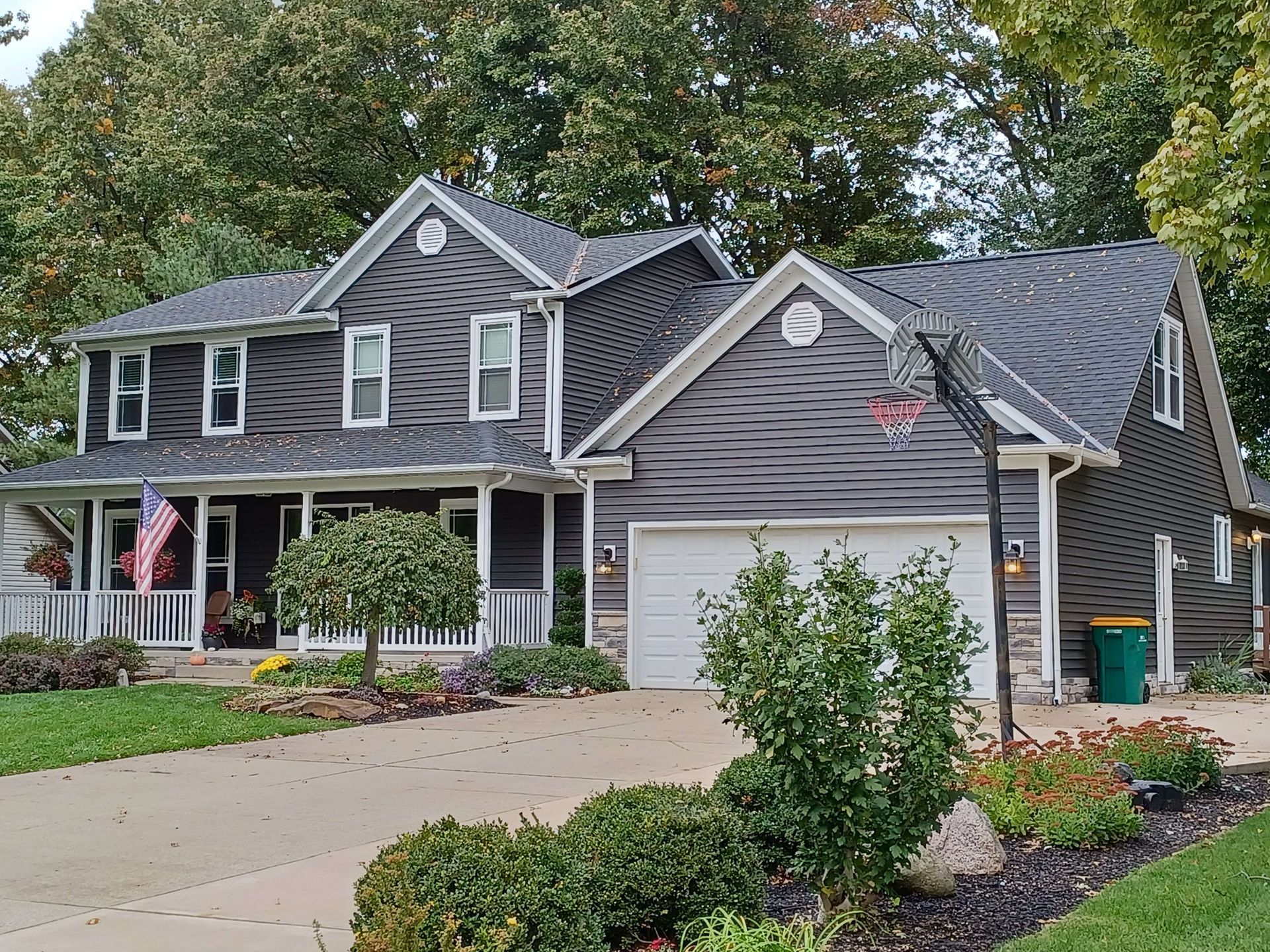 Two-story gray house with white trim, front porch, garage, and landscaped yard on a suburban street
