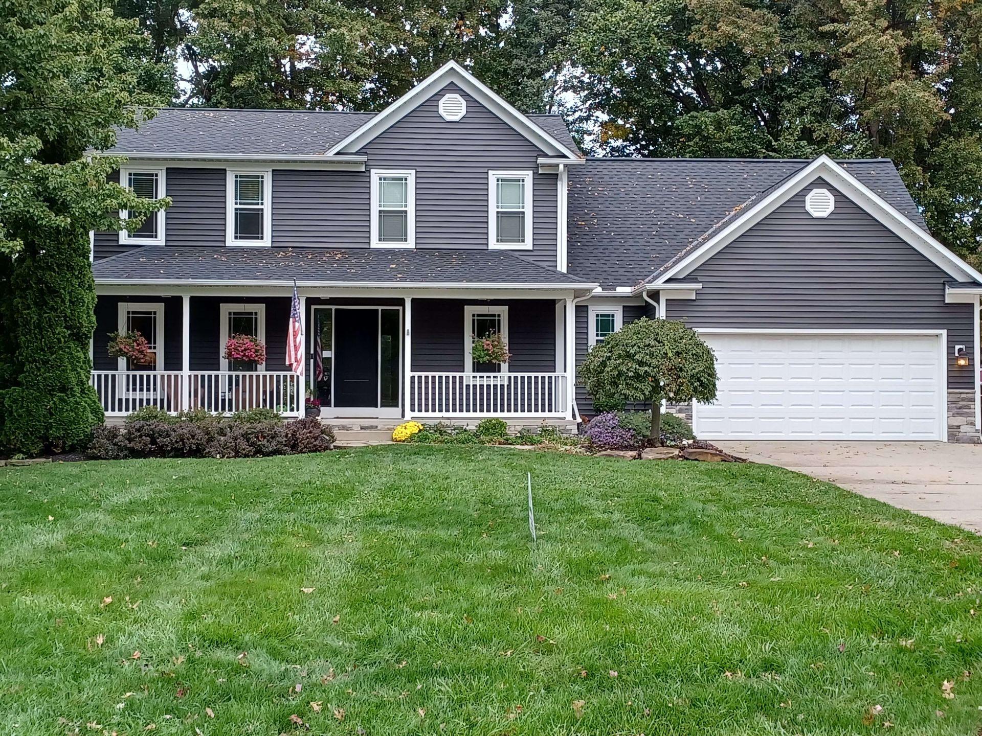 Gray two-story suburban house with front porch, white trim, attached garage, and a green lawn