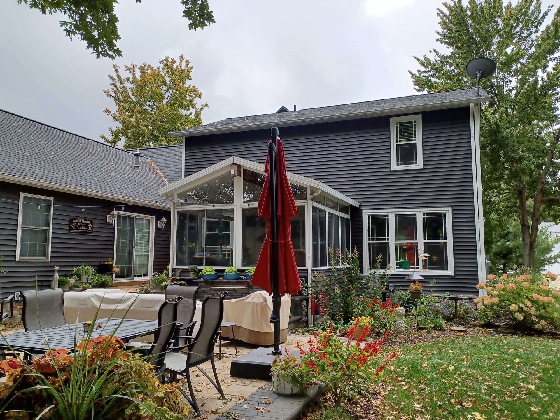A black house with a screened in porch and a red umbrella in front of it.
