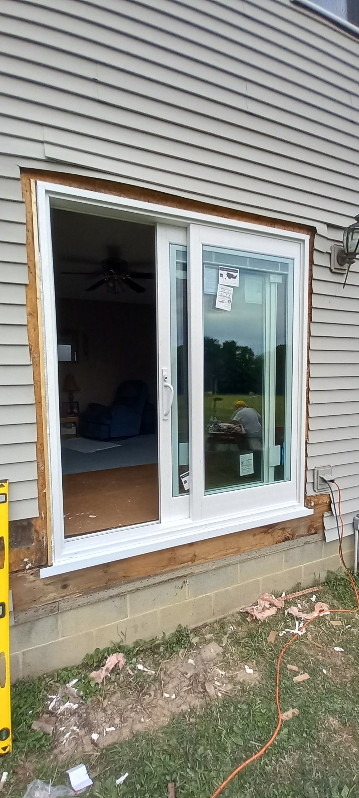 Partially installed white sliding glass door on a house exterior with exposed framing and siding