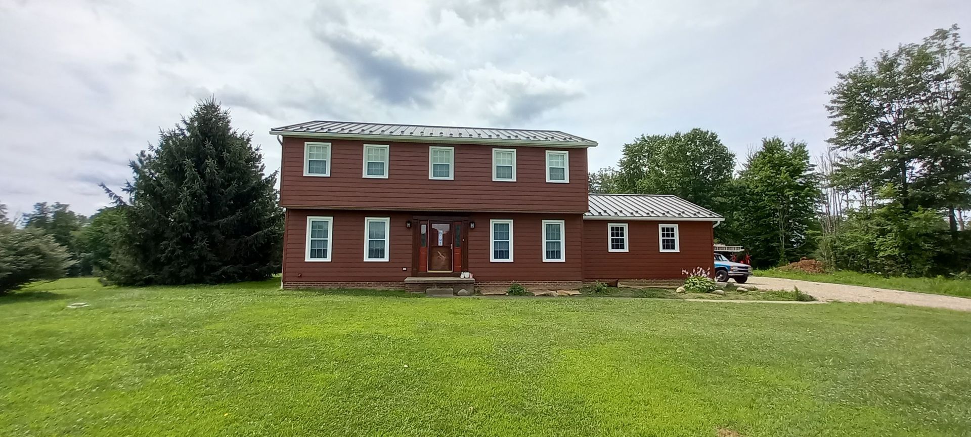 Two-story red brick house with white trim and a large green lawn under a cloudy sky