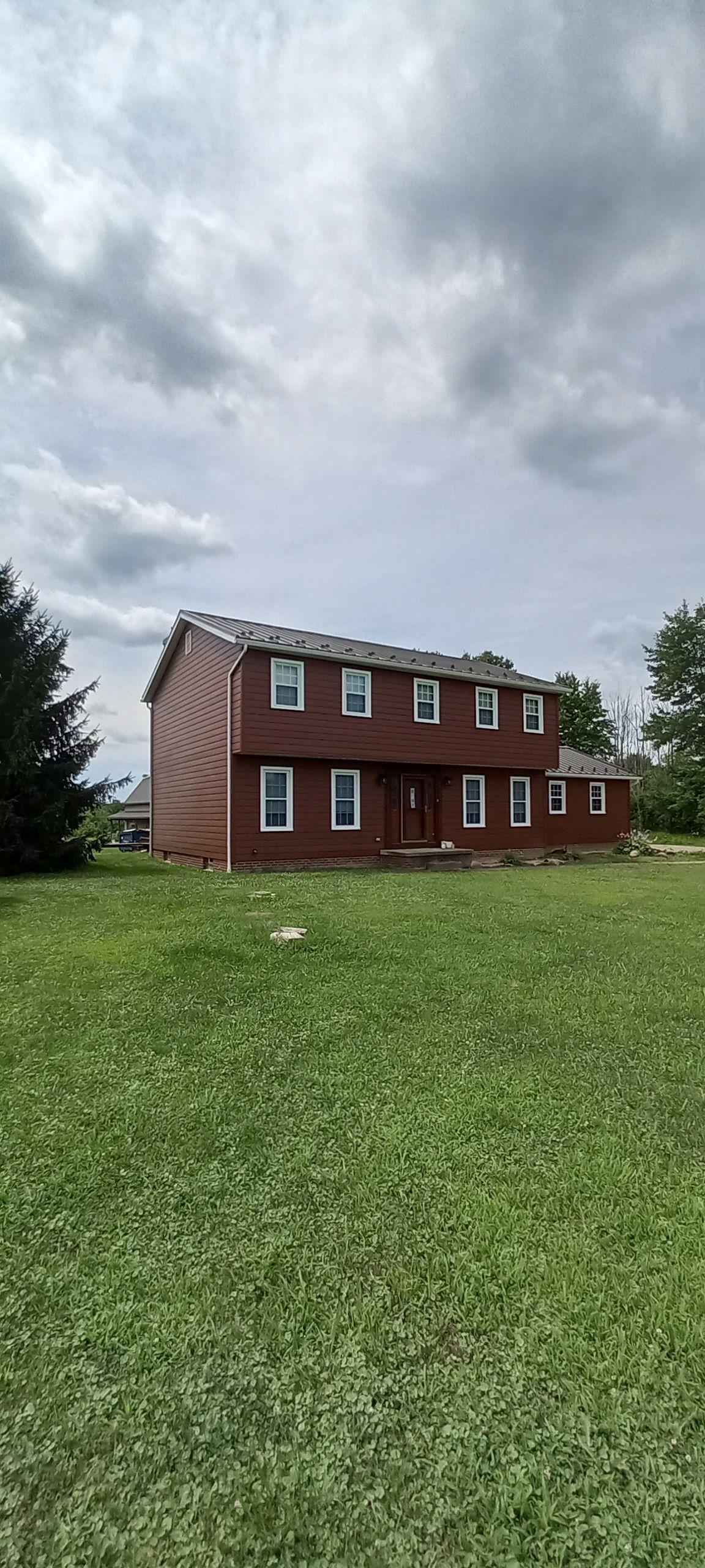 Two-story red house with white-trimmed windows on a grassy lawn under a cloudy sky