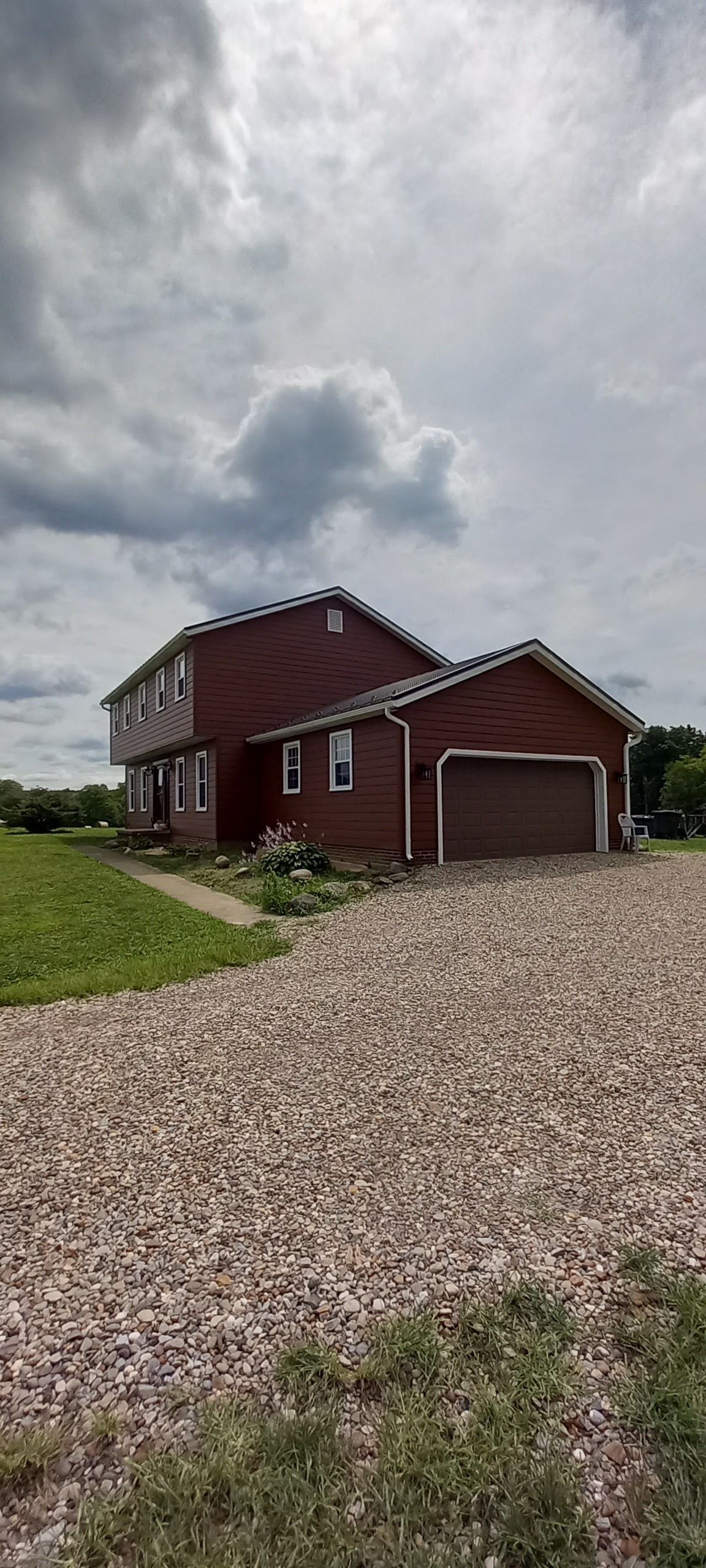 Red house with gravel driveway under a cloudy sky in a rural setting