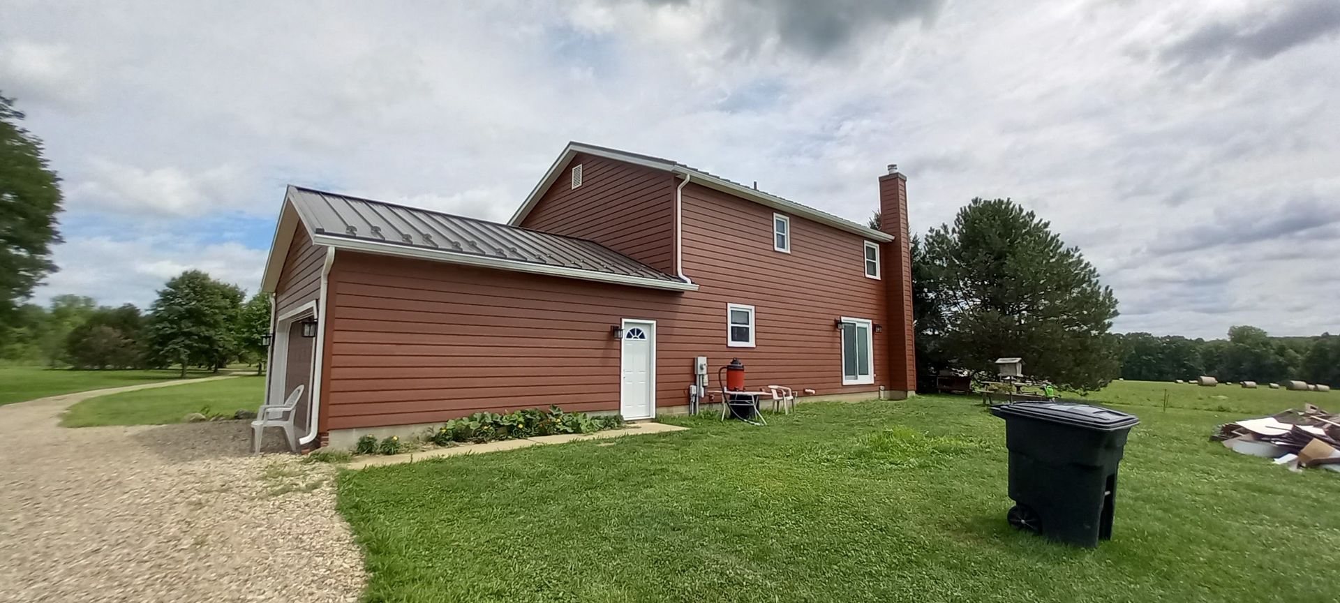 Red barn-style house with white trim on a grassy rural lot under a cloudy sky
