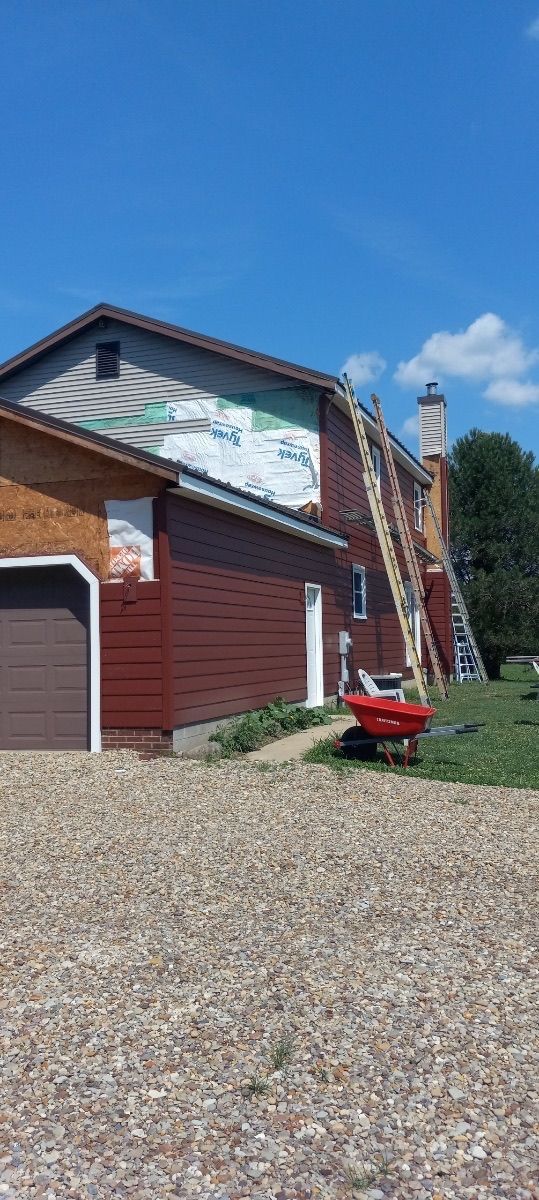 Red house with a garage, blue ladder on the roof, and a red wheelbarrow on a gravel driveway.