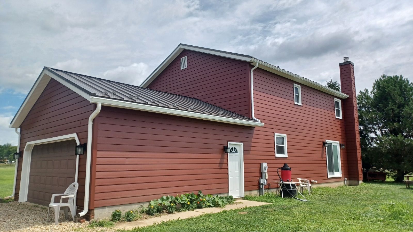 Red two-story house with attached garage, white trim, and green lawn under a cloudy sky