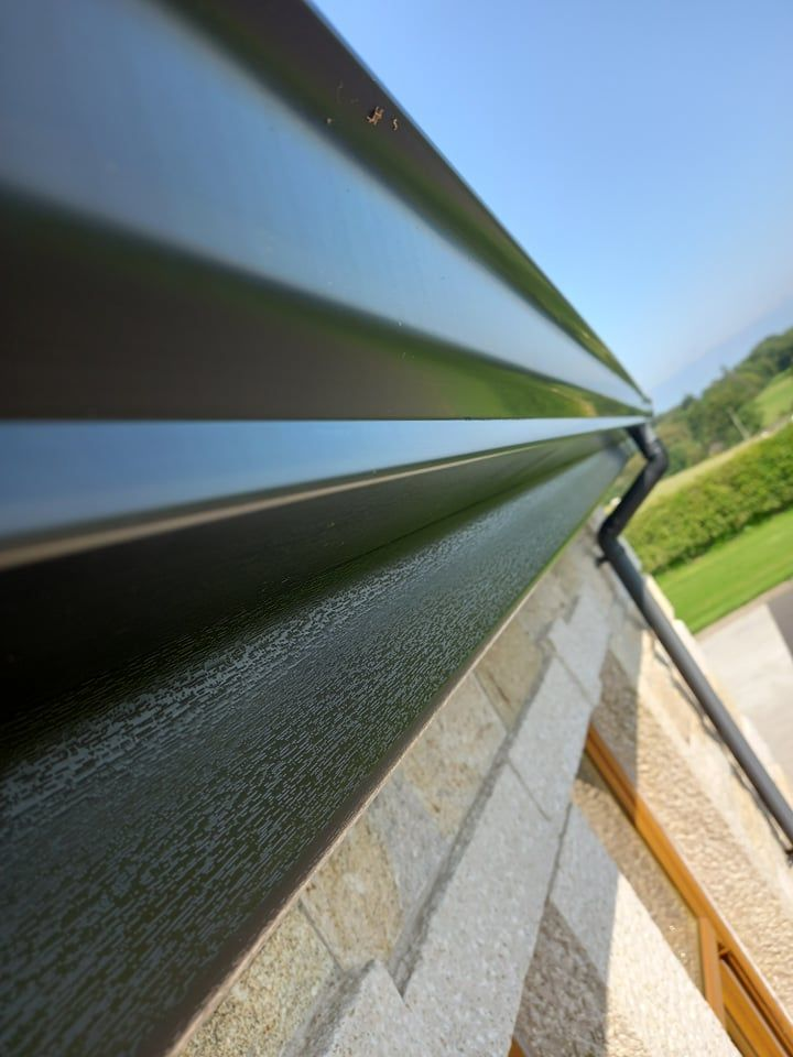 Close view of dark seamless aluminium guttering and fascia on a stone fronted house, fitted by CVG